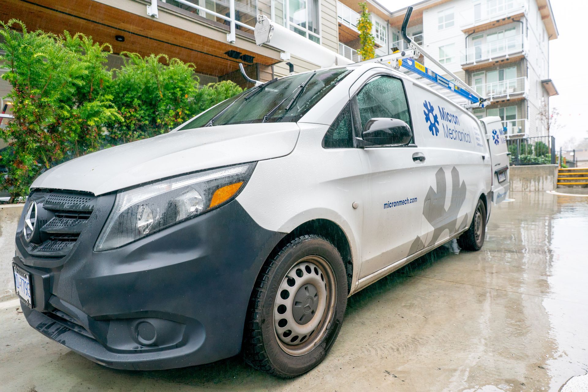 Air conditioner unit outside a brown house near a wooden deck and foliage.