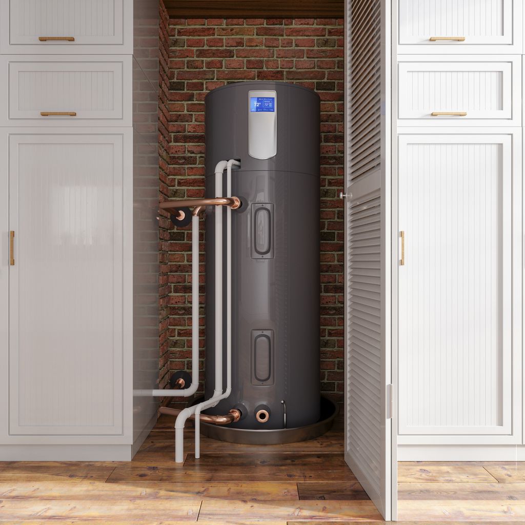A gray heat pump water heater in a utility closet with white cabinets and exposed brick.