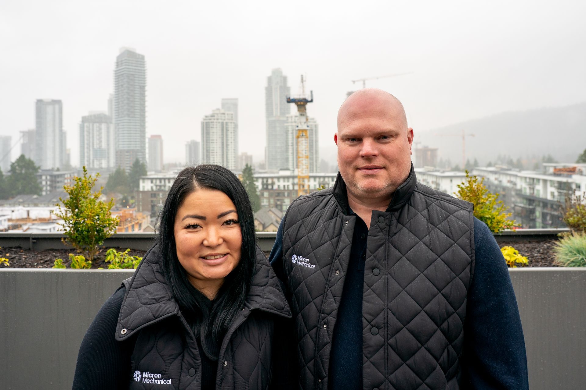 Two workers wearing safety vests examine a document outdoors near a ladder and wall.