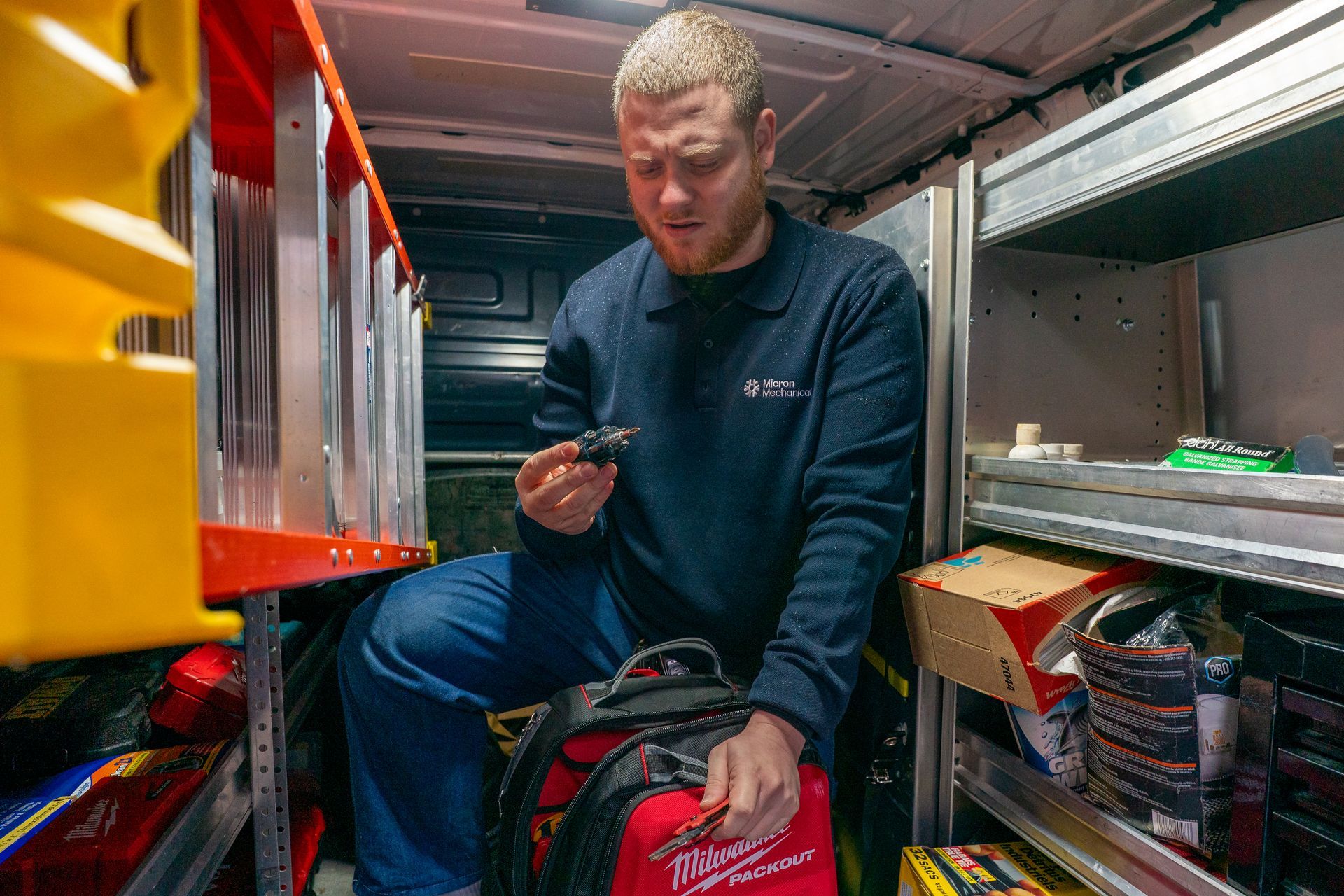 Air conditioner unit outside a brown house near a wooden deck and foliage.