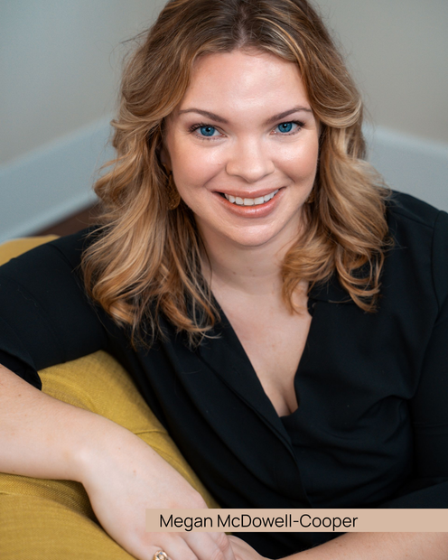 Woman with blonde hair, sitting at a desk with a laptop, smiling and resting her chin on her hand.