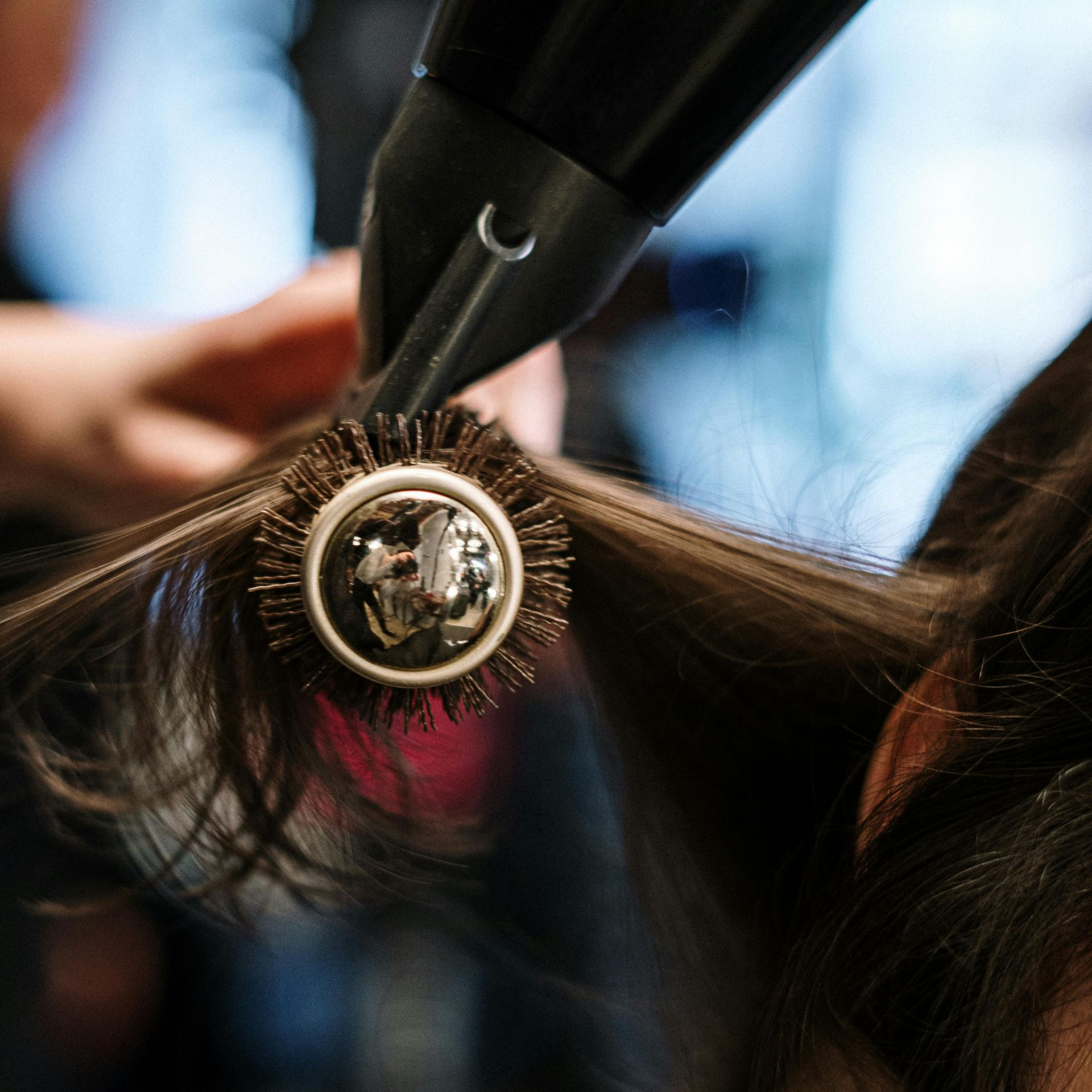 Hairdresser blow-drying hair with round brush. Dark hair, close-up.