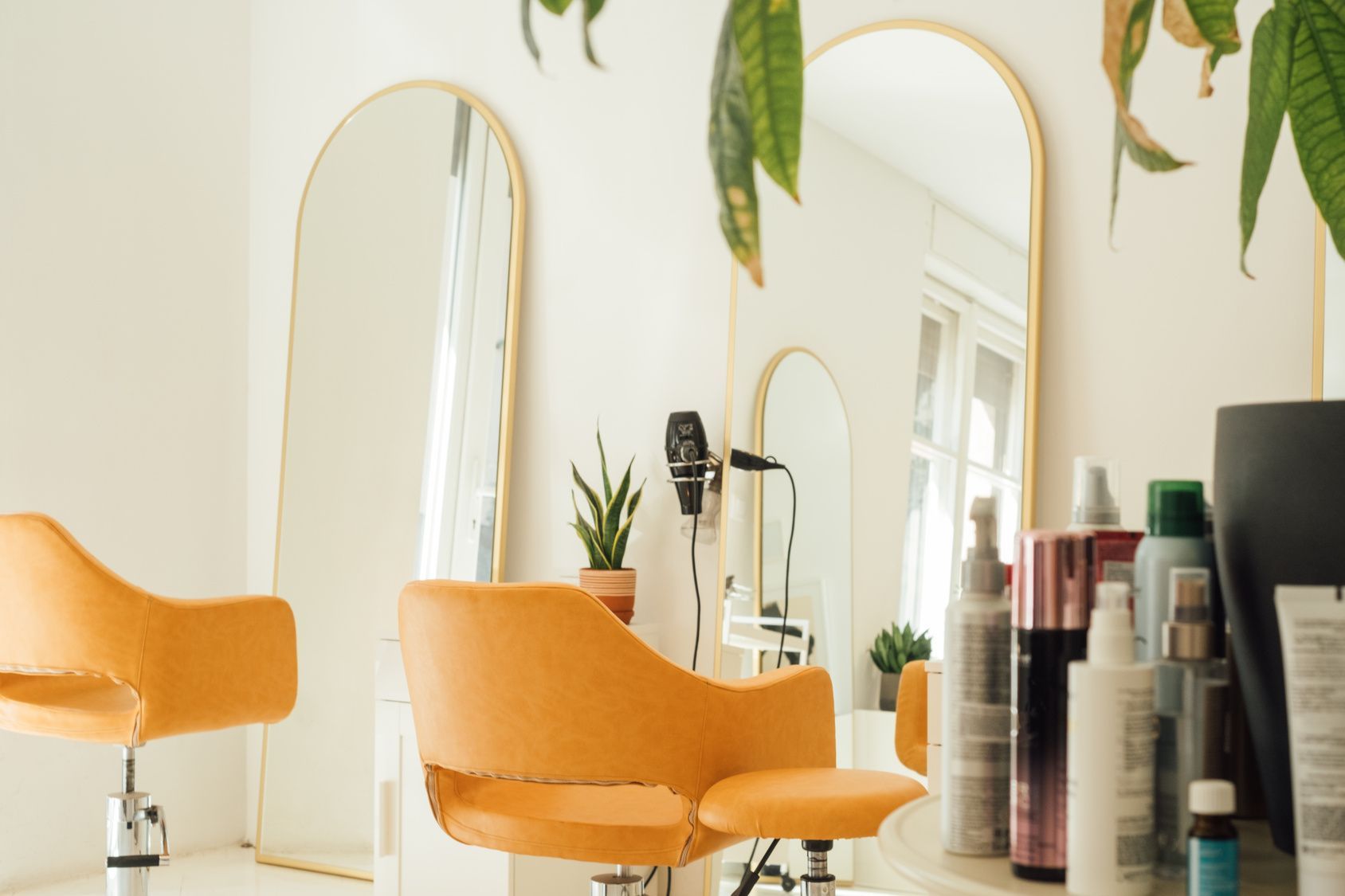 Hair salon interior with orange chairs, arched mirrors, and hair products.