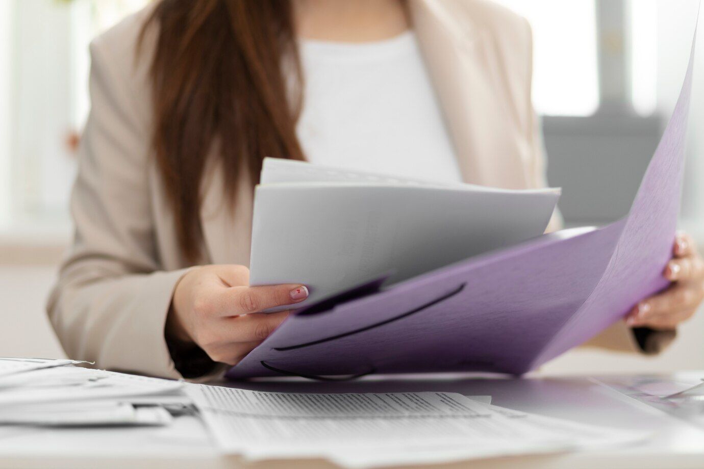 A woman is sitting at a desk holding a purple folder and a piece of paper.