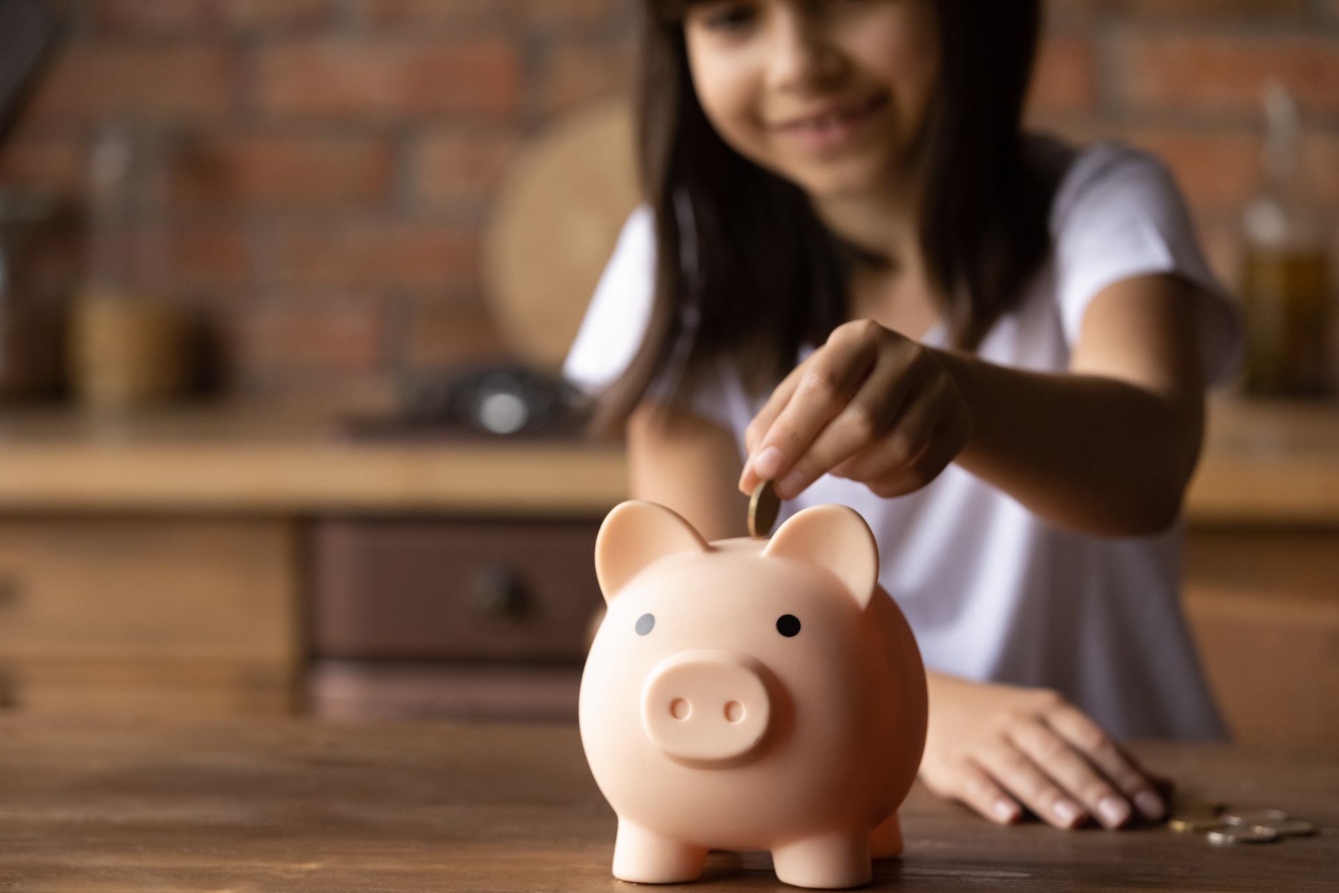 A little girl is putting coins into a piggy bank.