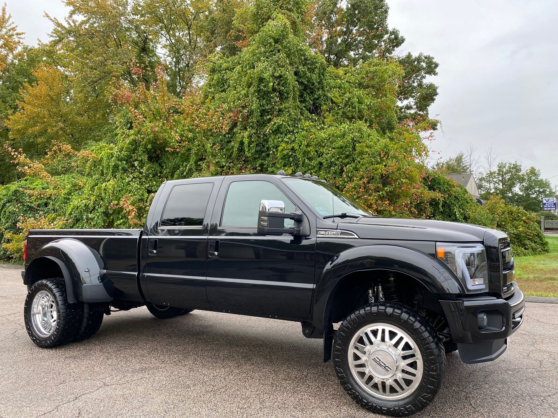 a black pickup truck is parked on a gravel road in front of trees .