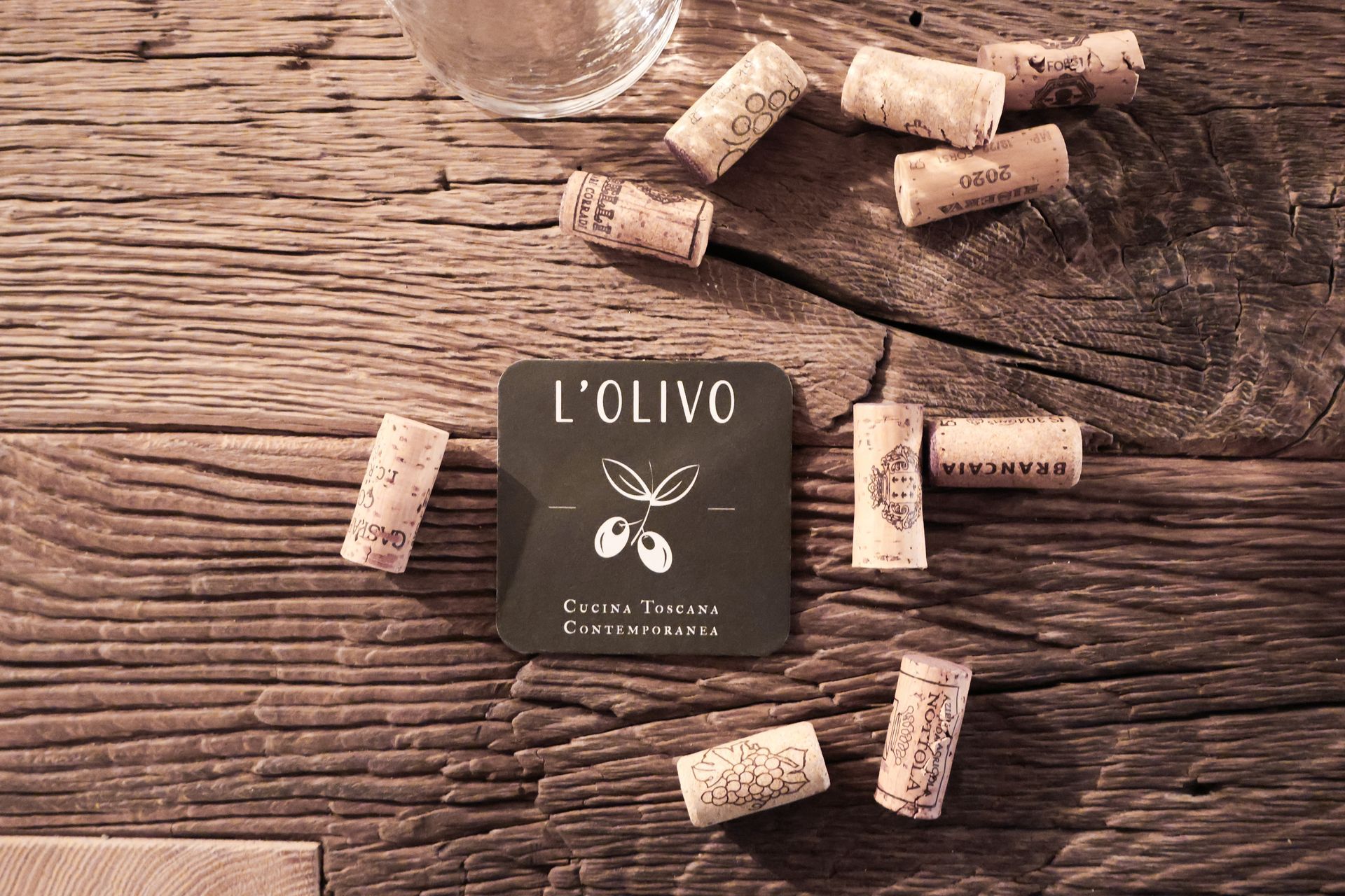 A wooden table with corks and a coaster that says l' olivo