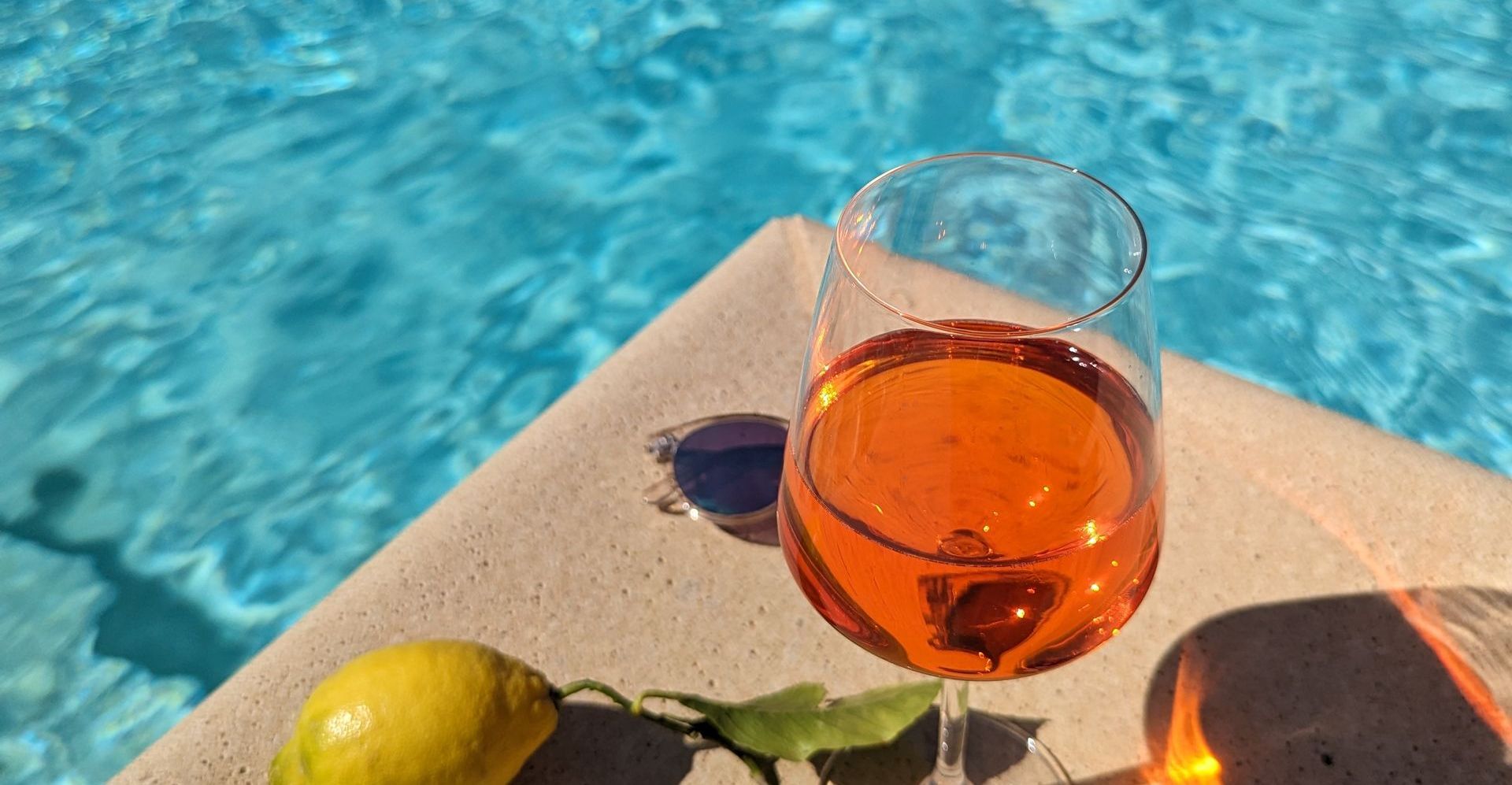 A glass of wine is sitting on a ledge next to a swimming pool.