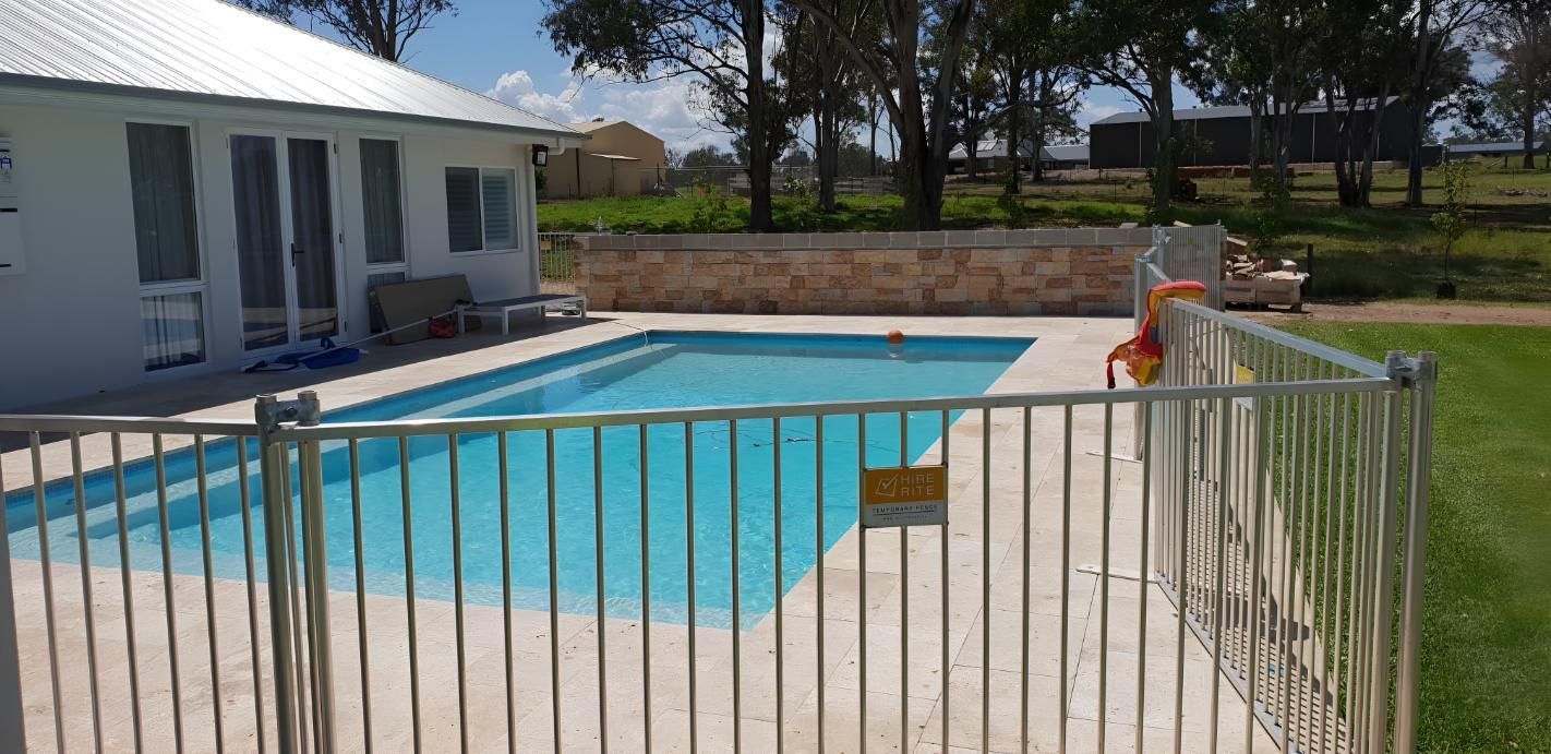 A Fence Surrounds A Large Swimming Pool In Front Of A House — Lewis Landscapes In Yippin Creek, NSW