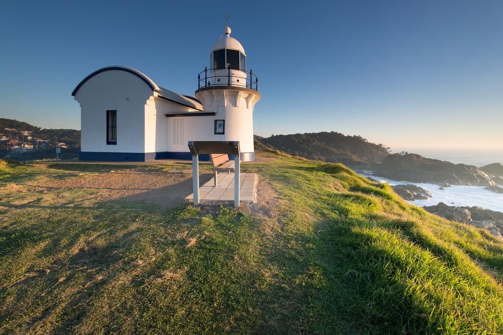 A Lighthouse Is Sitting On Top Of A Grassy Hill Overlooking The Ocean — Lewis Landscapes In Port Macquarie, NSW