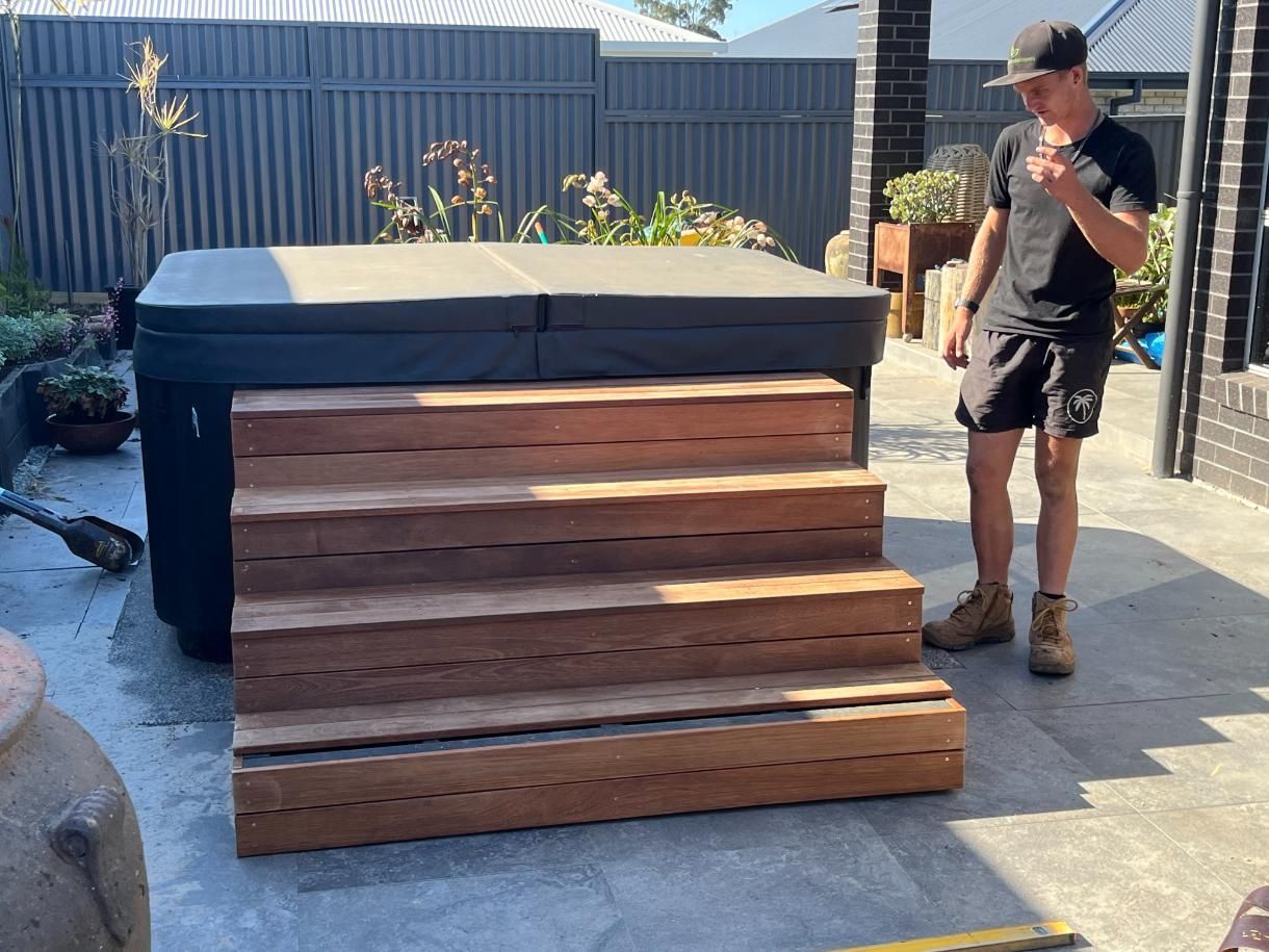 A Man Is Standing Next To A Wooden Staircase In Front Of A Hot Tub — Lewis Landscapes In Yippin Creek, NSW