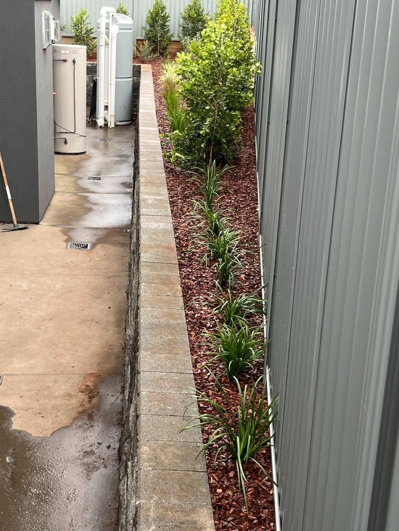 A Sidewalk Next To A Fence With Plants Growing On It — Lewis Landscapes In Yippin Creek, NSW