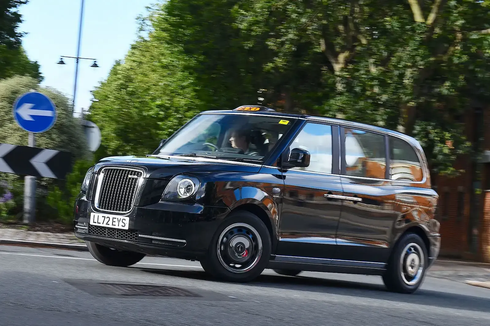 A black taxi cab is driving down a street