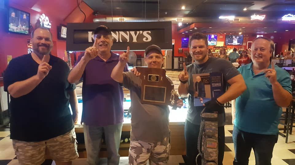 Five men posing at a pool hall under a