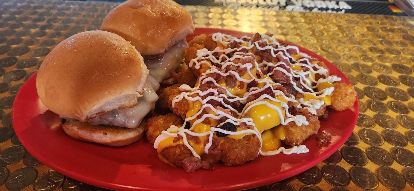 Two small burgers and a large serving of loaded tater tots with cheese, bacon, and drizzle on a red plate.