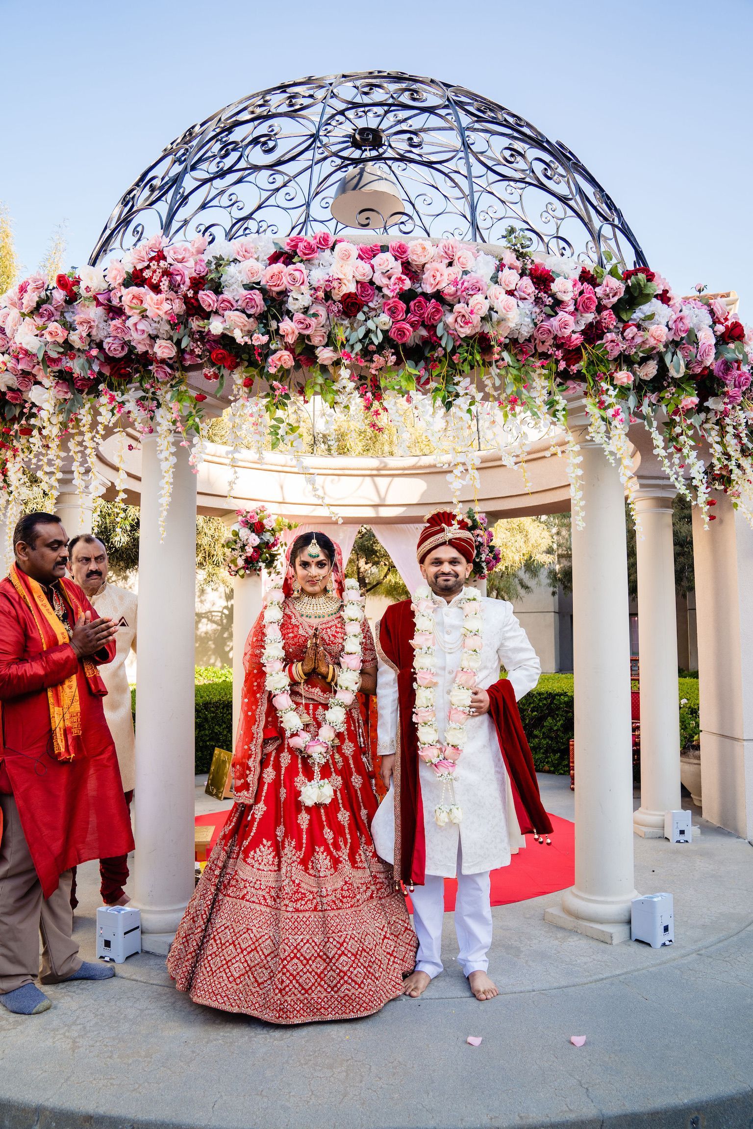 Indian couple in wedding attire under floral archway.
