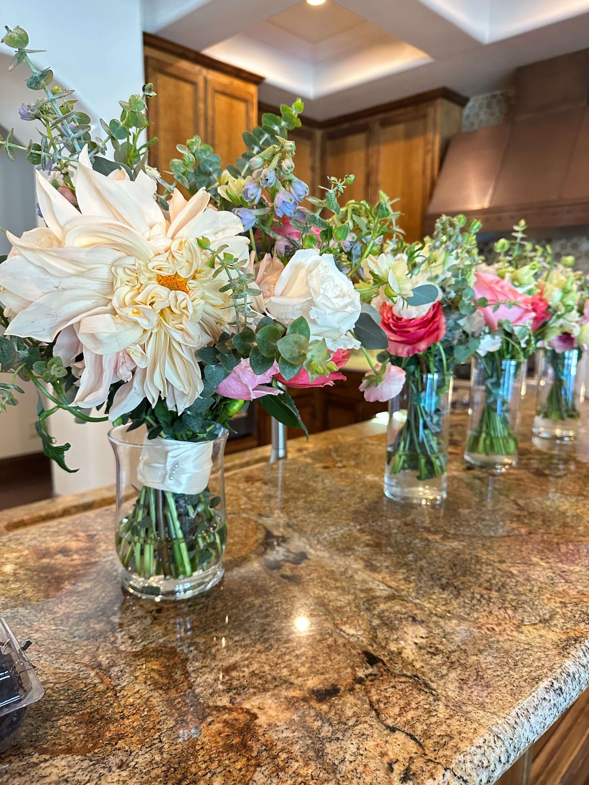 Bouquets of colorful flowers in glass vases arranged on a granite countertop in a kitchen.