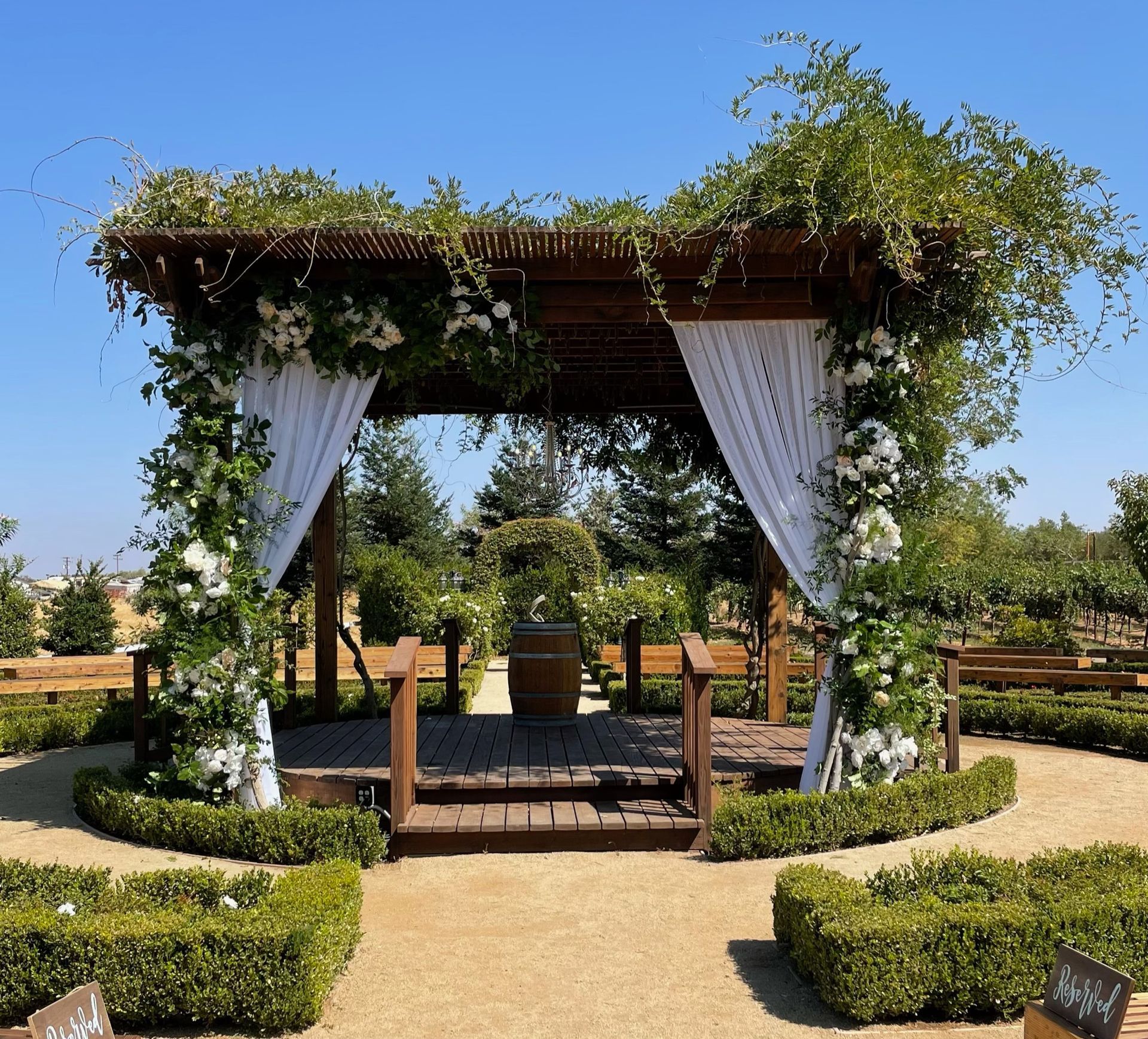 Wooden pergola decorated with white flowers and draping fabric, in a garden.