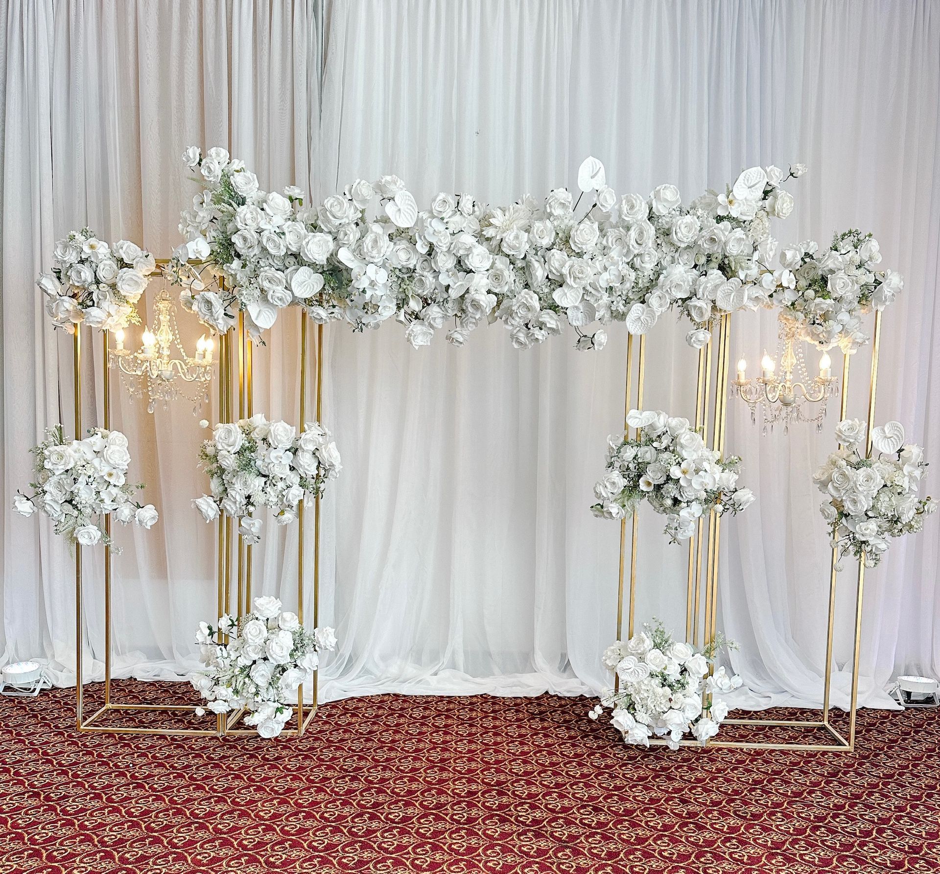 Gold floral arch decorated with white flowers against white draped backdrop.