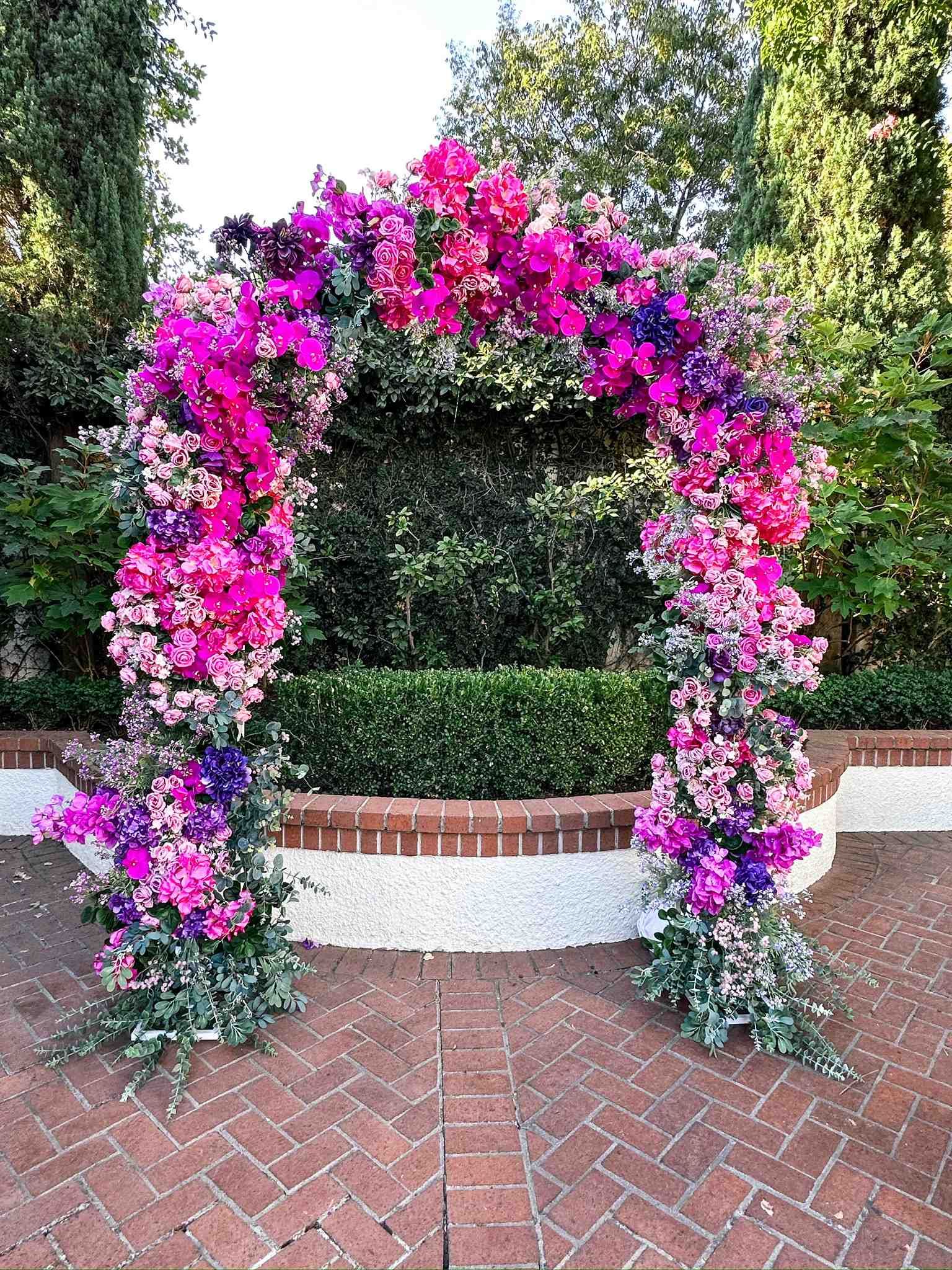 Floral archway with pink, purple, and magenta flowers, set against green foliage.