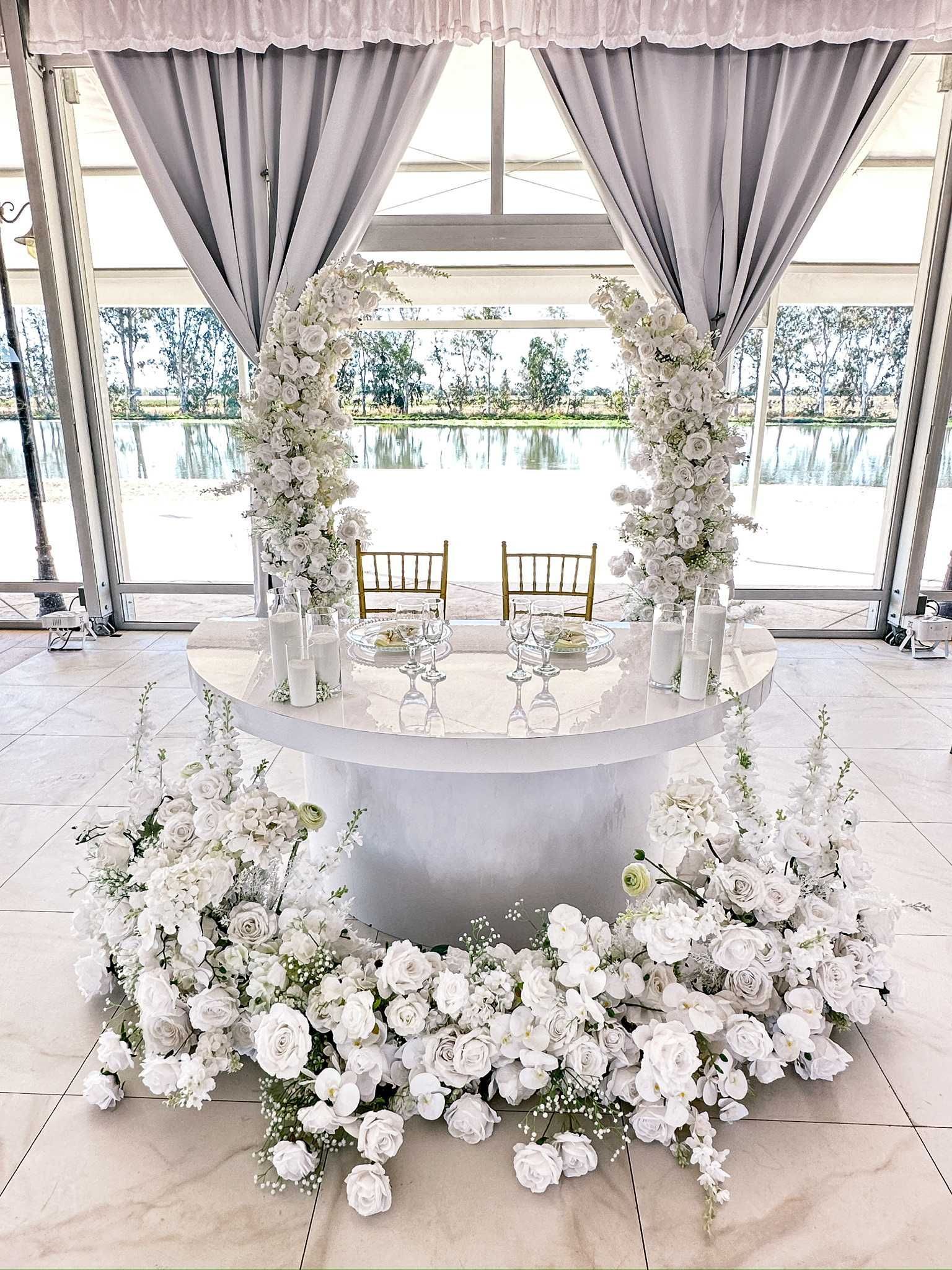 Wedding reception setup with white flowers, drapes, and a round table.