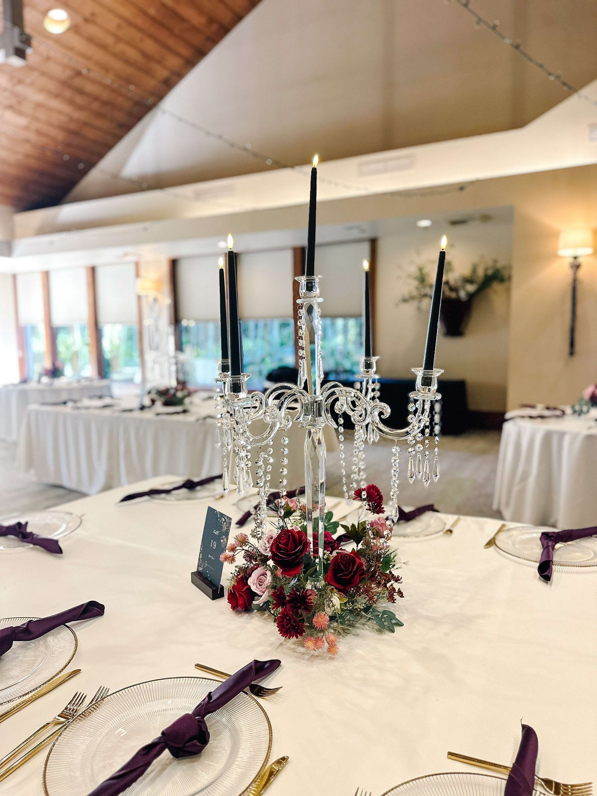Table setting with candelabra centerpiece, black candles, and floral arrangement. White tablecloth, burgundy napkins.