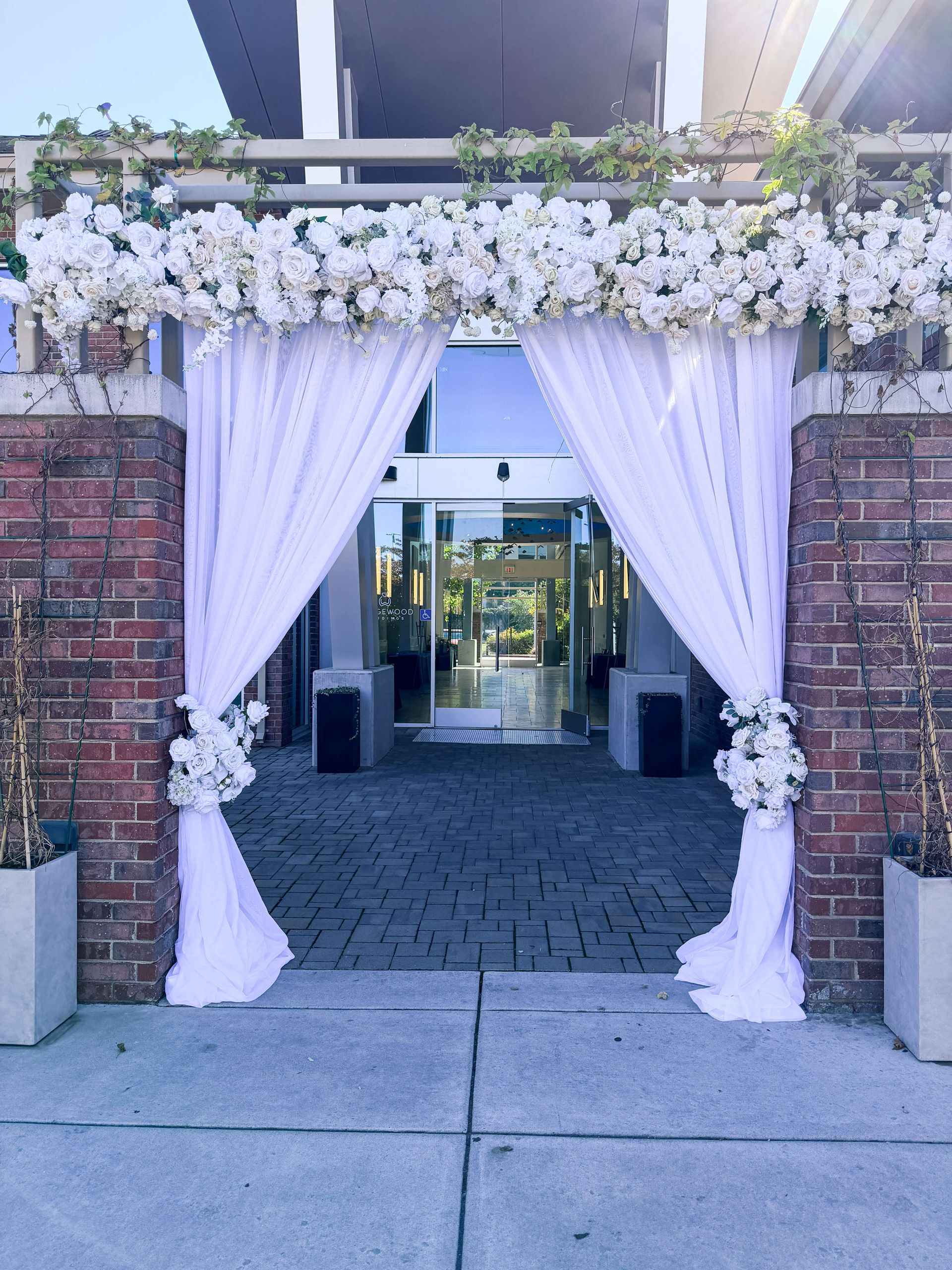 White draped entrance decorated with white flowers. Brick wall.