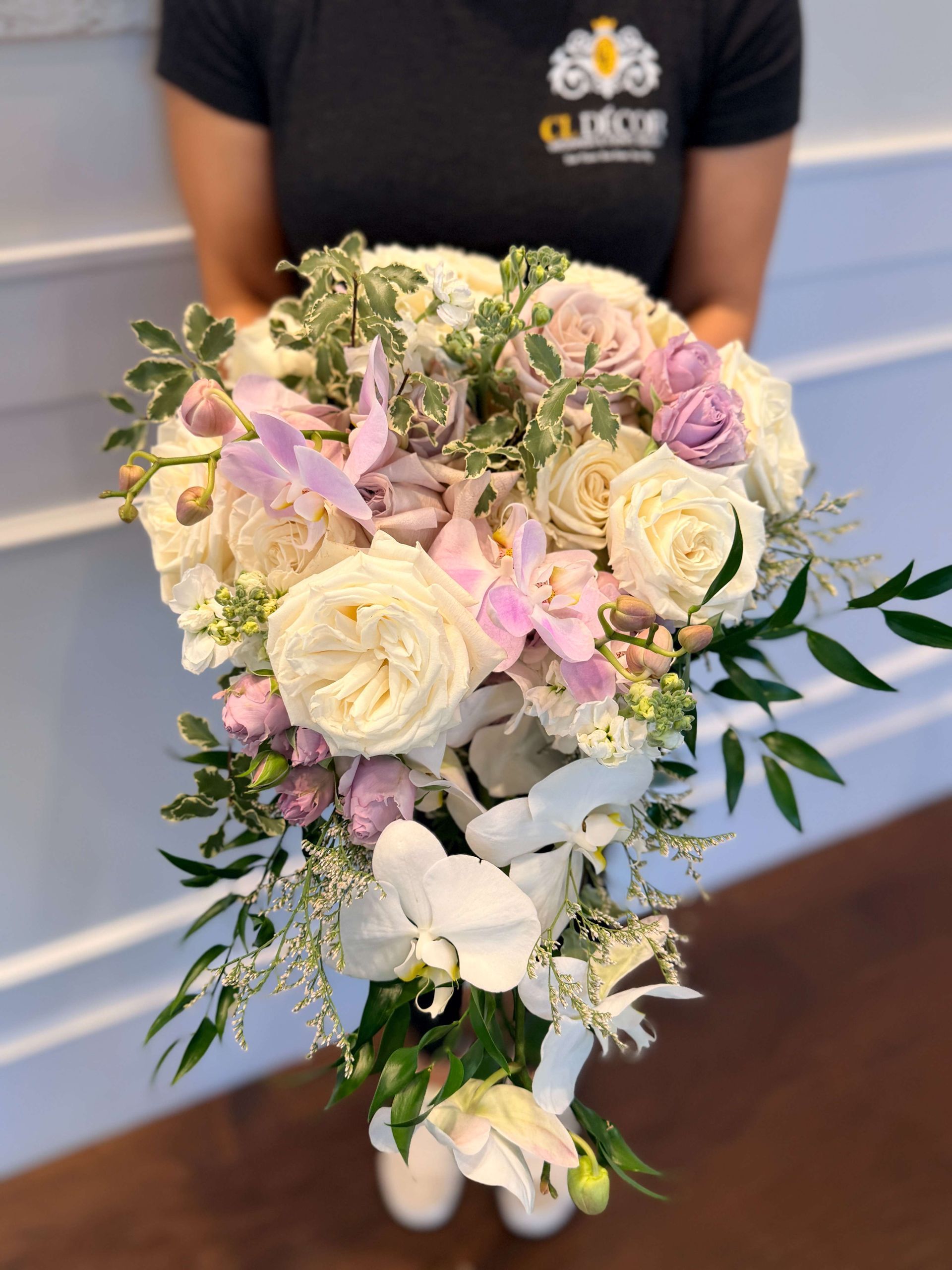 Woman holding a cascading bouquet of white, cream, and lavender flowers with greenery.