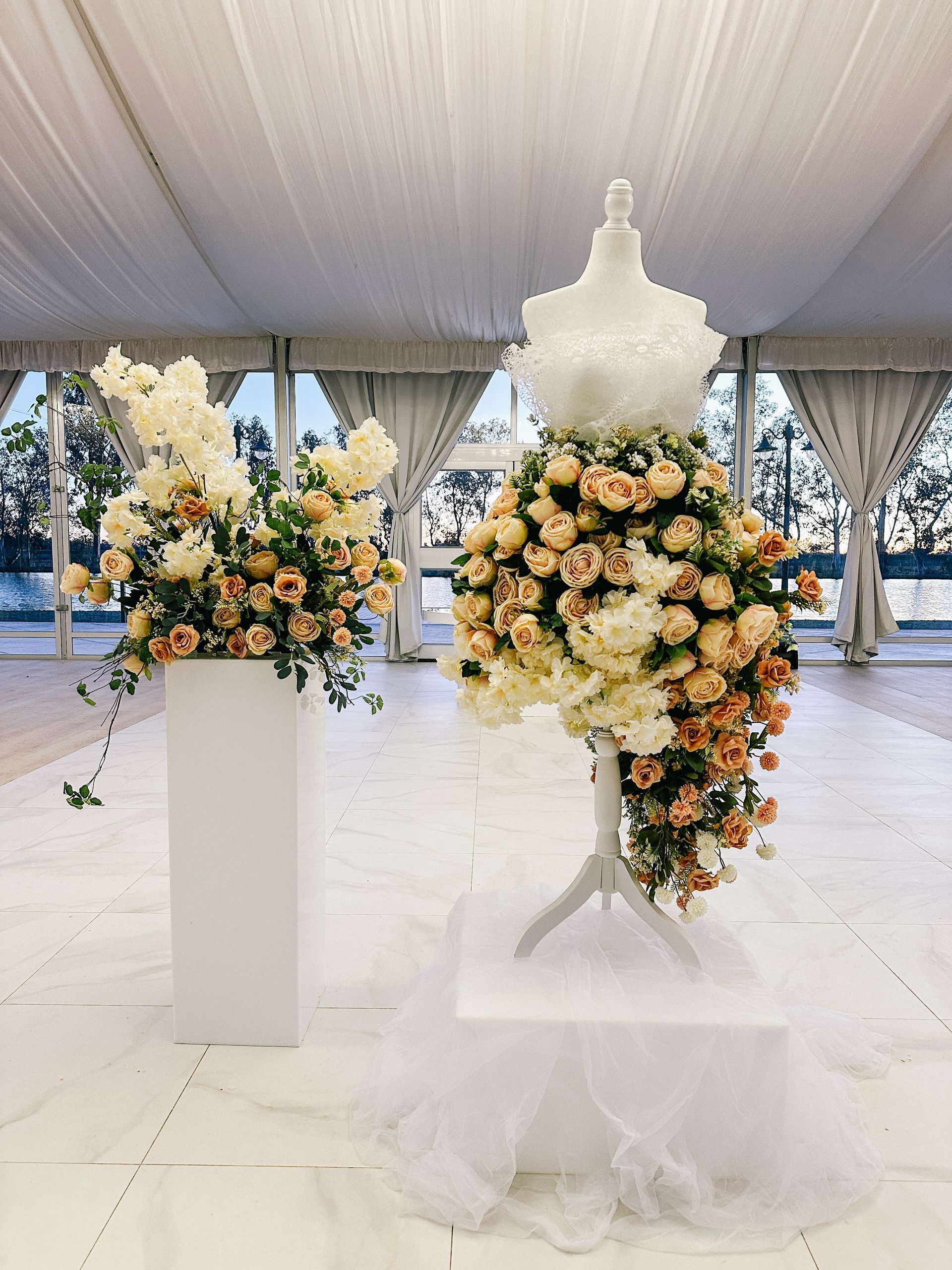 Floral display featuring a mannequin in a dress of peach and white flowers next to a column of flowers.