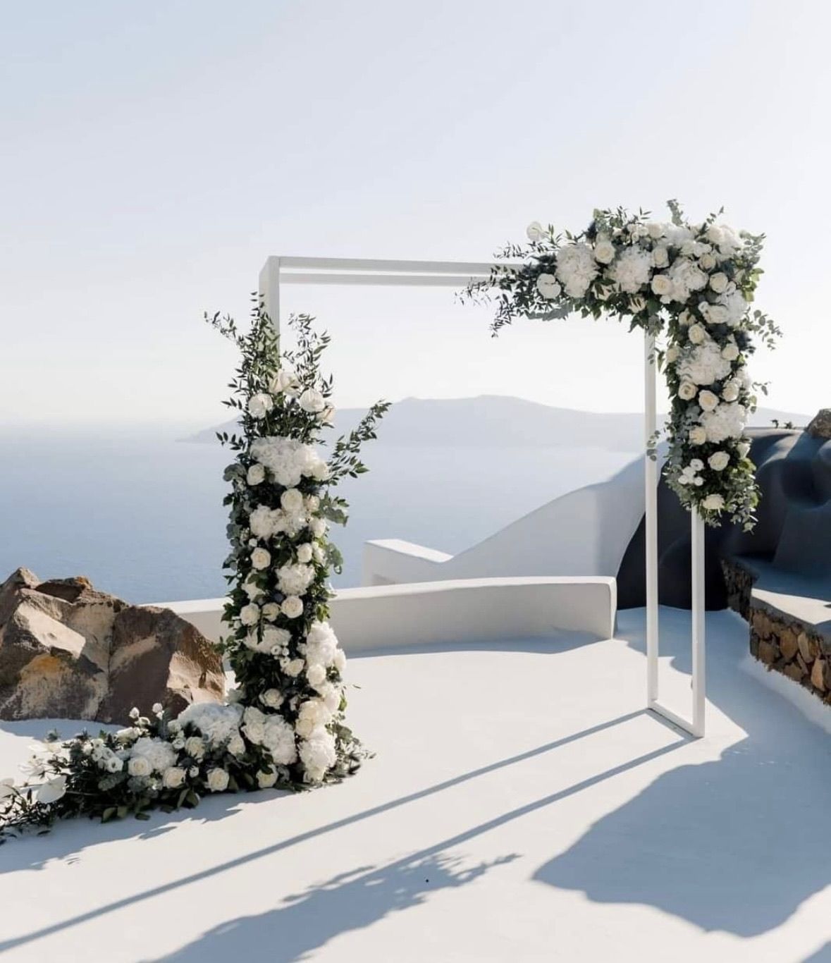 White floral wedding arch overlooking a blue sea and landscape.