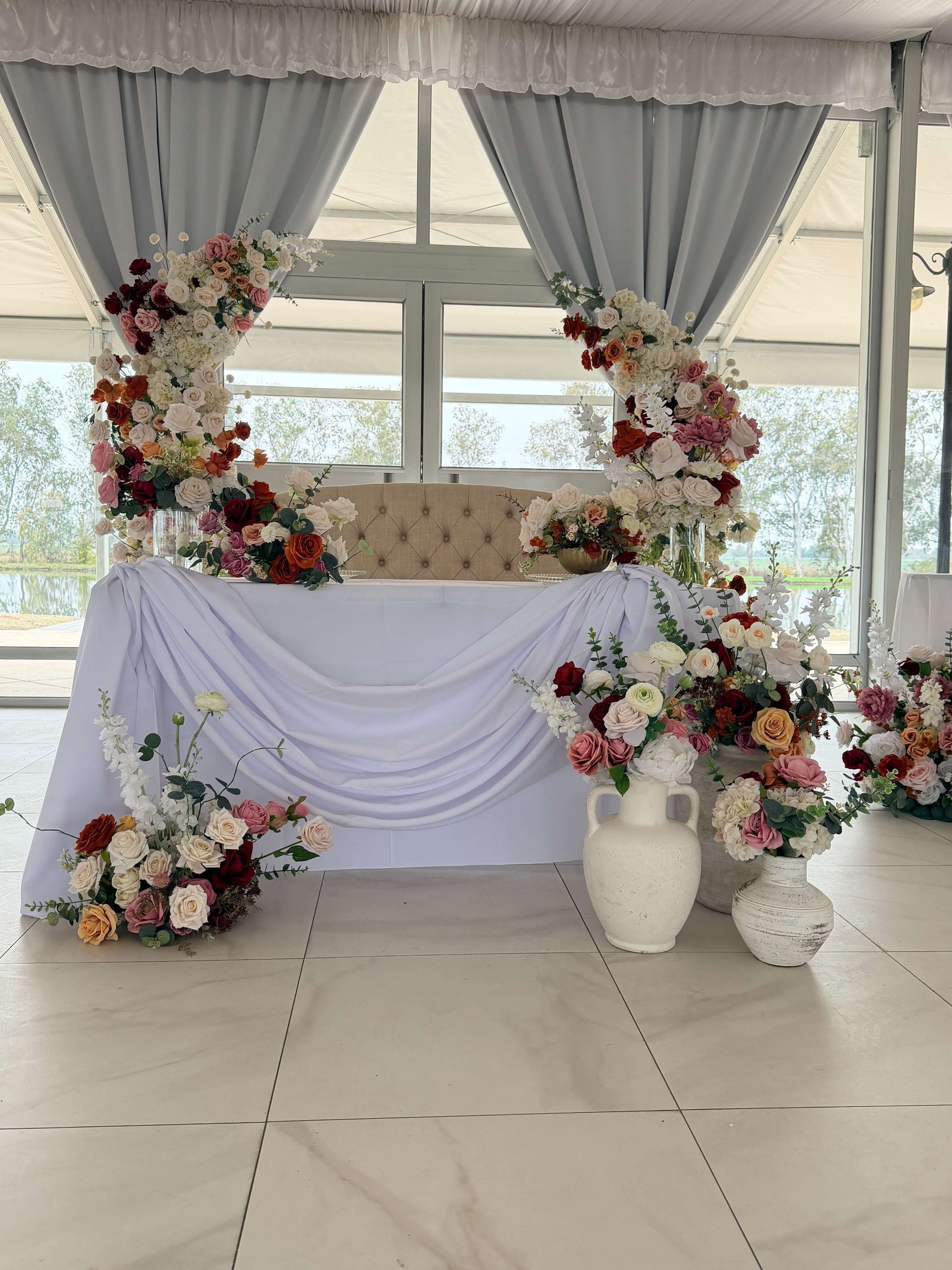 Wedding reception decor: floral arches around a table draped in white fabric, with vases of flowers.