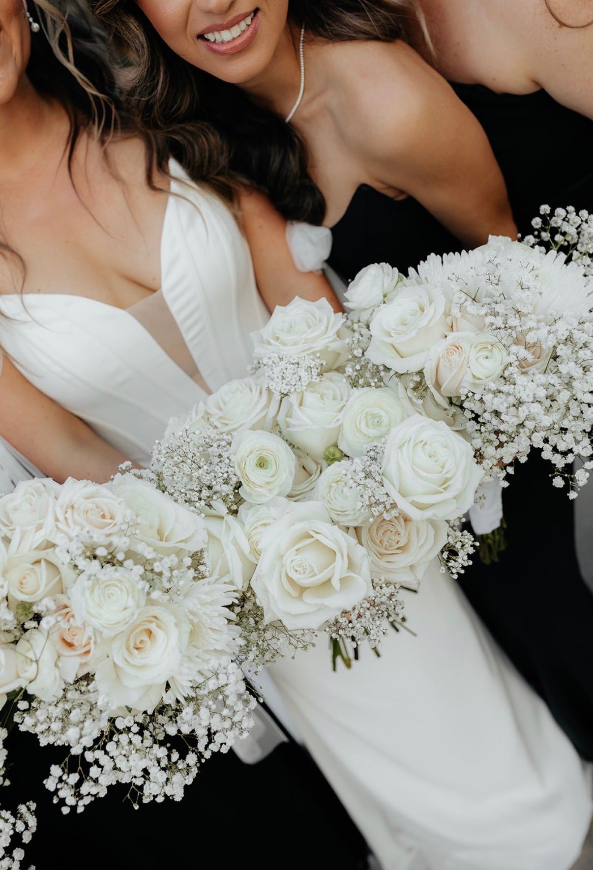 Bridesmaids in white dresses hold white rose bouquets; close-up view.