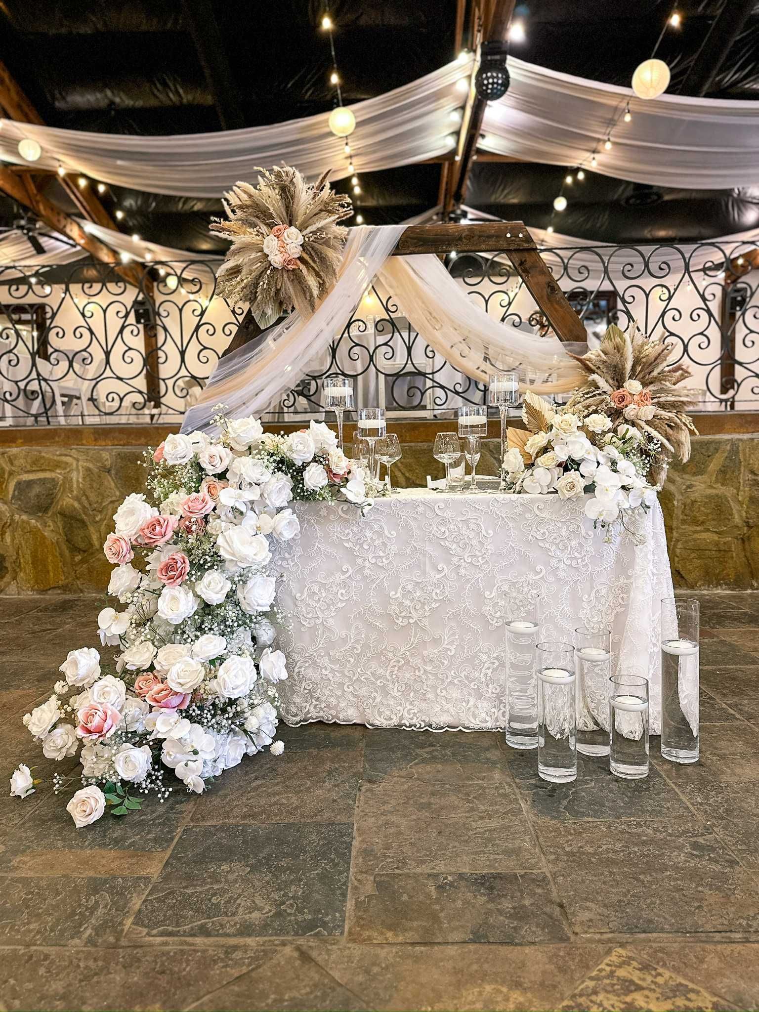 Wedding reception table decorated with white and pink flowers, and a draped backdrop.