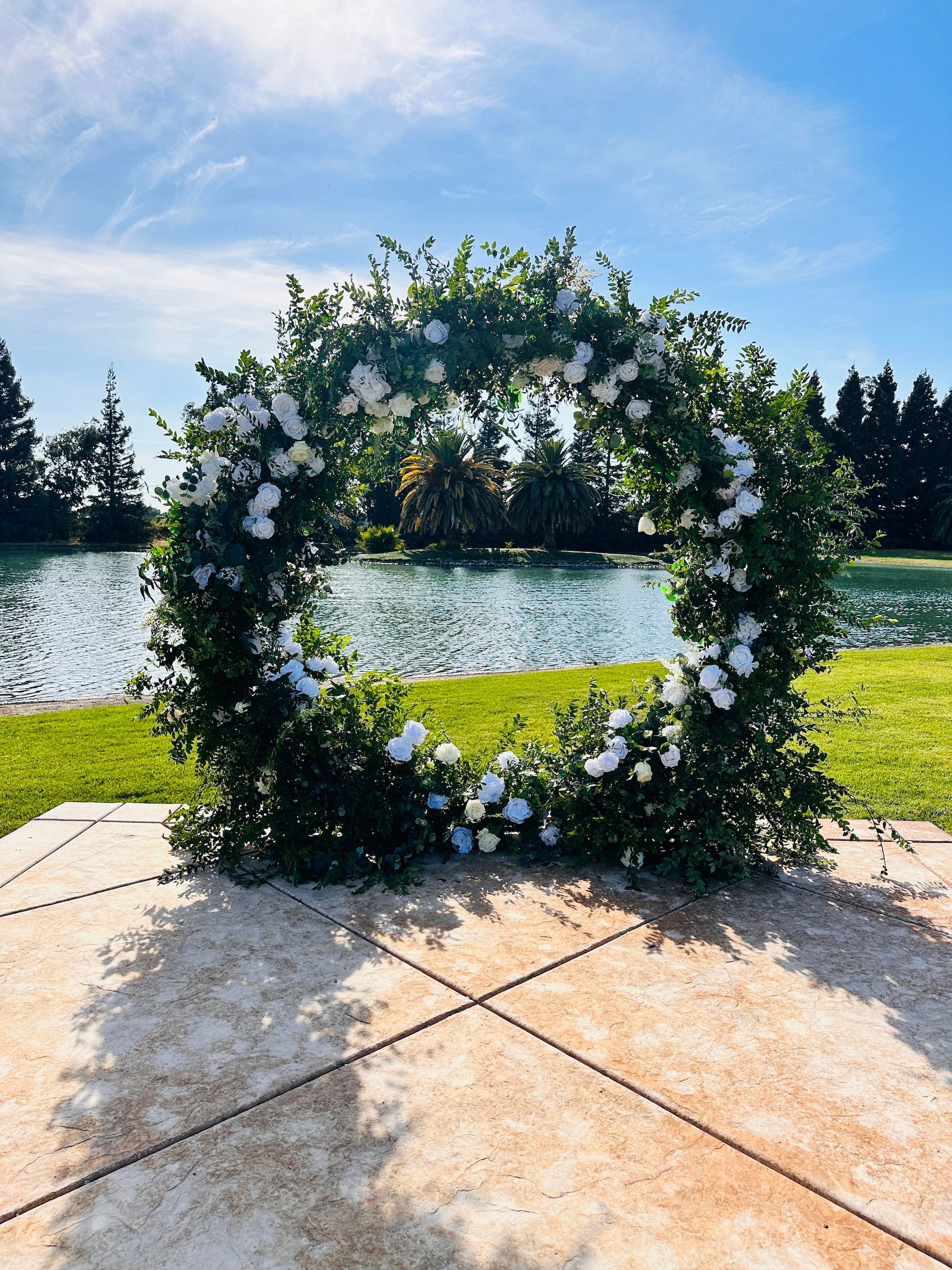 a wreath of white flowers is sitting on a patio in front of a lake and backdrop