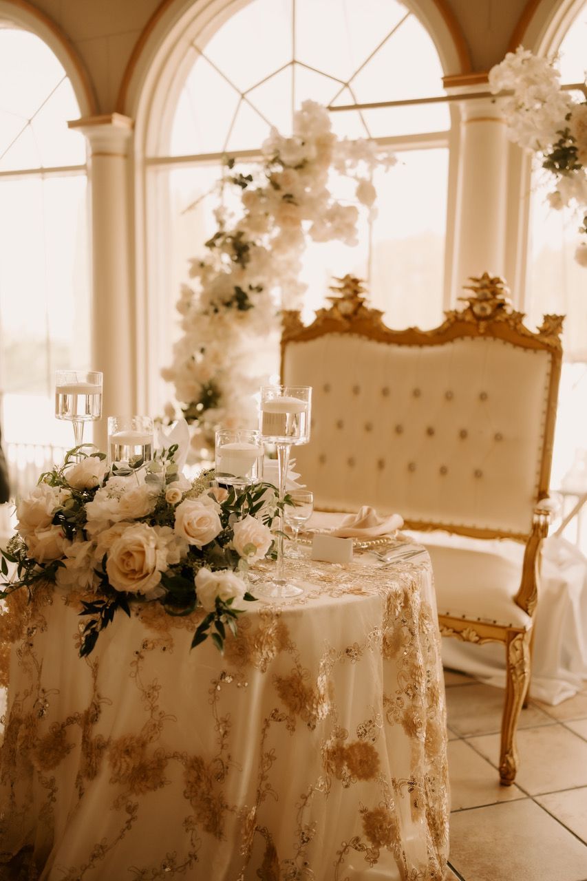 a table with a chair and flowers on it in front of a window and backdrop