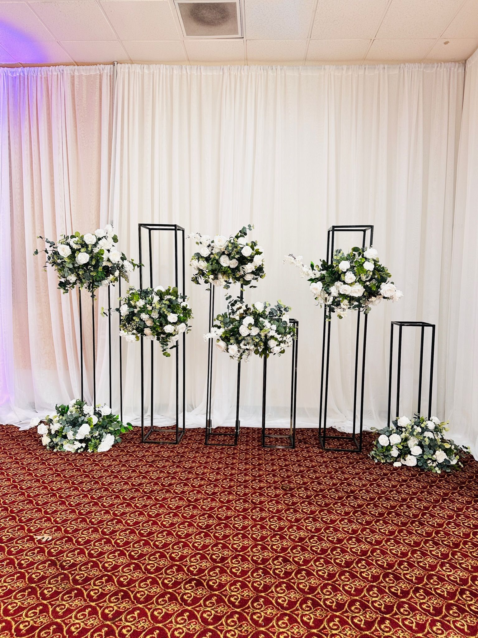 a room with a red carpet and white curtains and flowers on the floor and backdrop