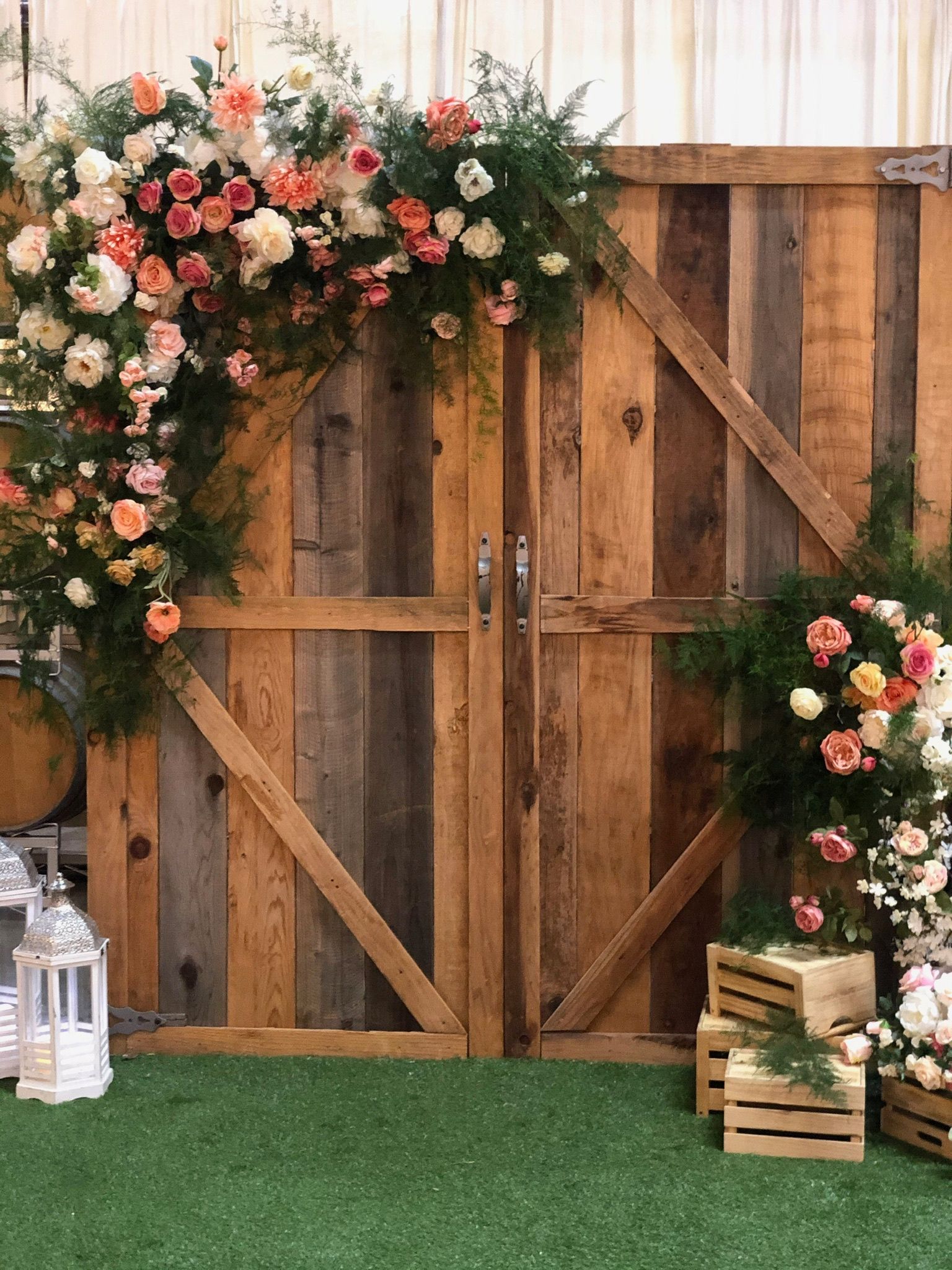 a wooden door decorated with flowers and lanterns is sitting on top of a lush green field and backdrop