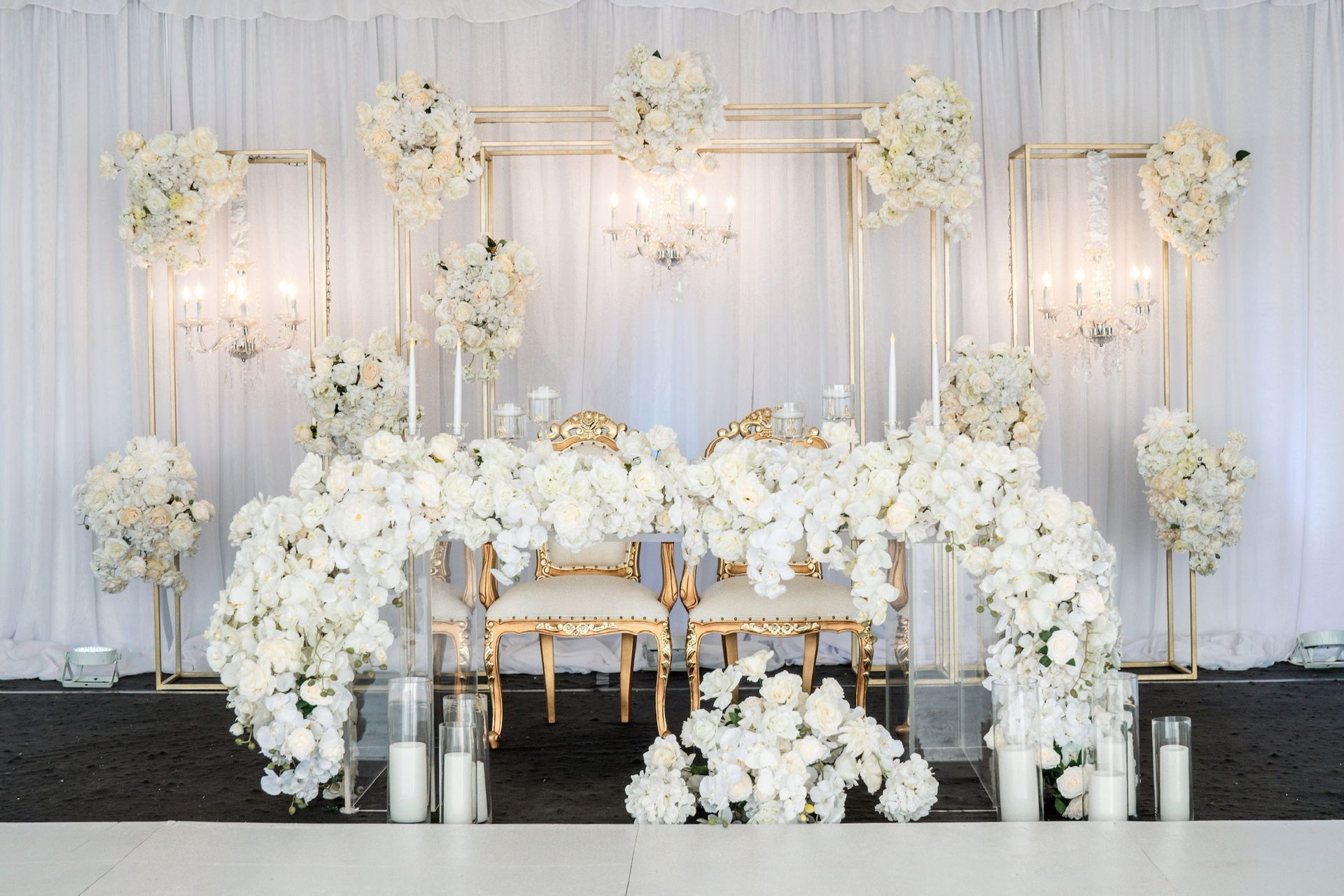 a wedding reception with a table and chairs decorated with white flowers and candles and backdrop .