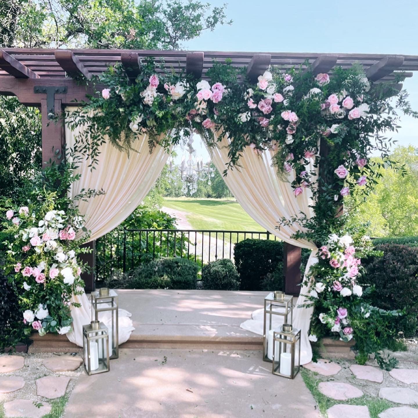 a wedding arch decorated with pink and white flowers and lanterns  and backdrop