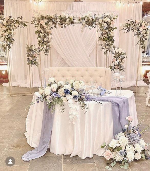 there is a table with flowers on it and a couch in the background with draping.