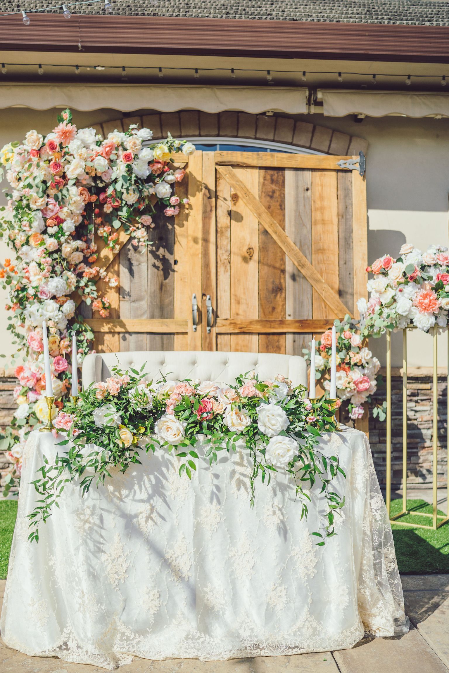 a wedding sweetheart table decorated with flowers and candles in front of a wooden door .