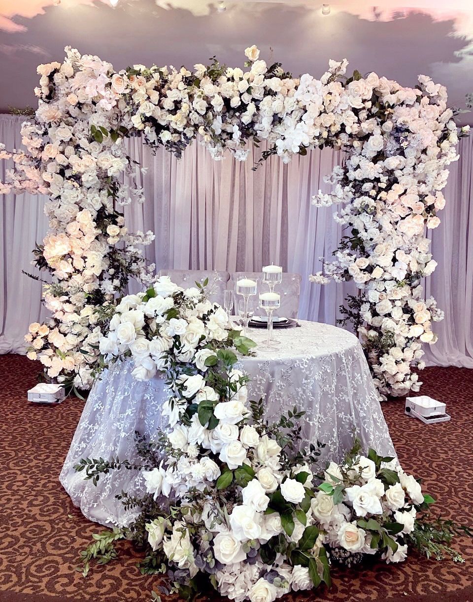 a sweetheart table is decorated with white flowers and a floral arch .