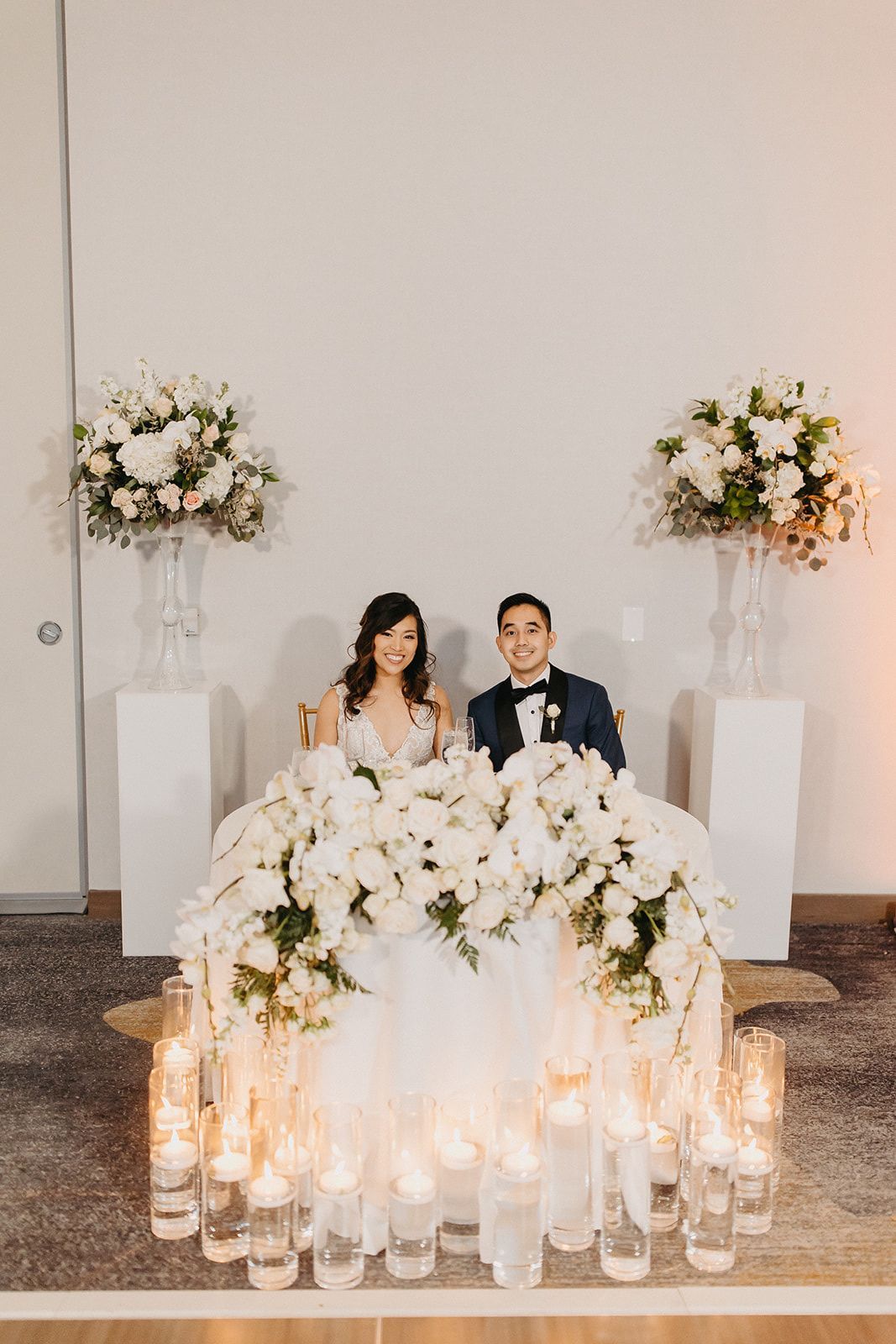 a bride and groom are sitting at a sweetheart table with candles and flowers .