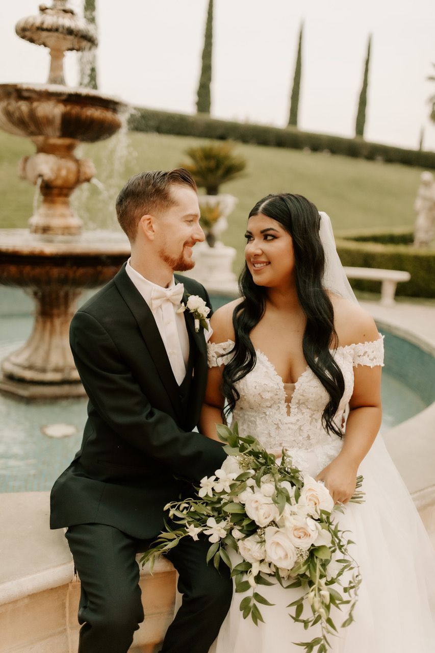 a bride and groom sit in front of a fountain