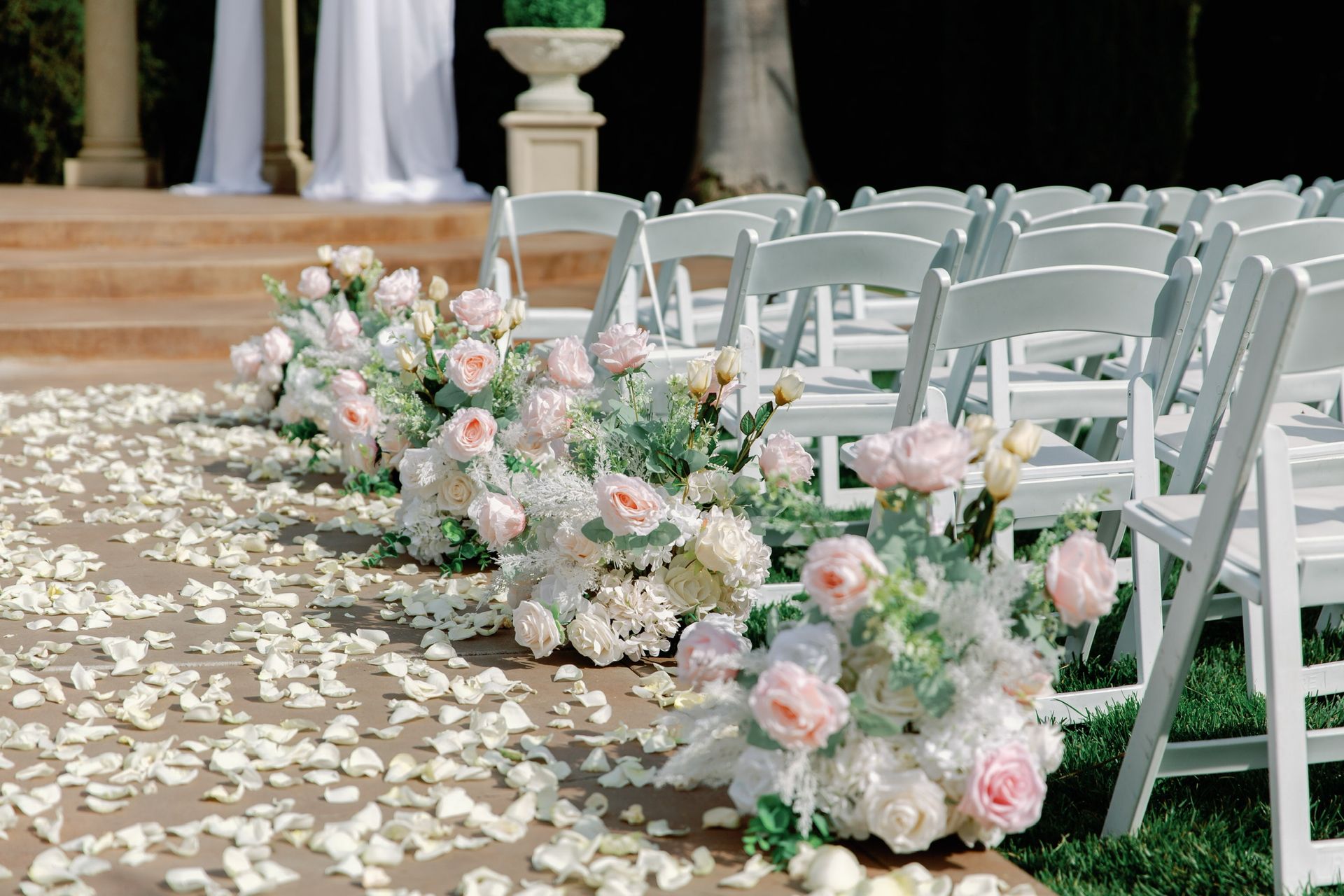 A row of white chairs lined up next to each other with flowers on the ground.