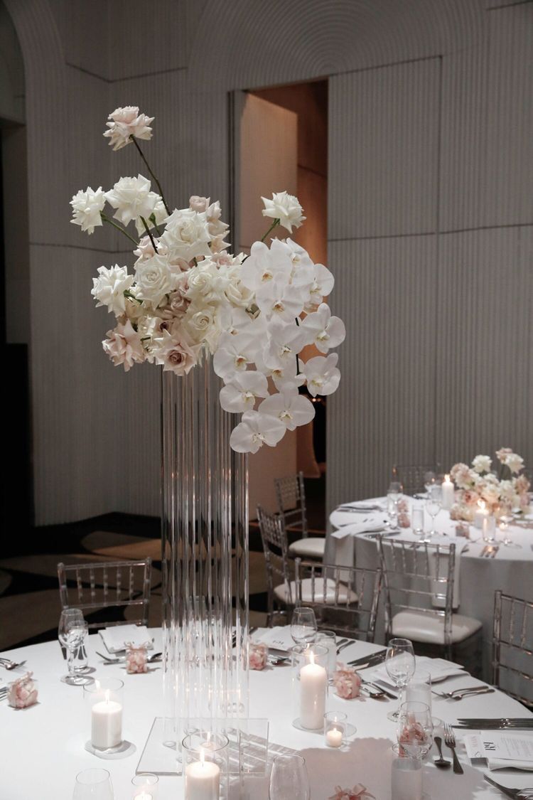 a clear vase with white flowers and candles on a table