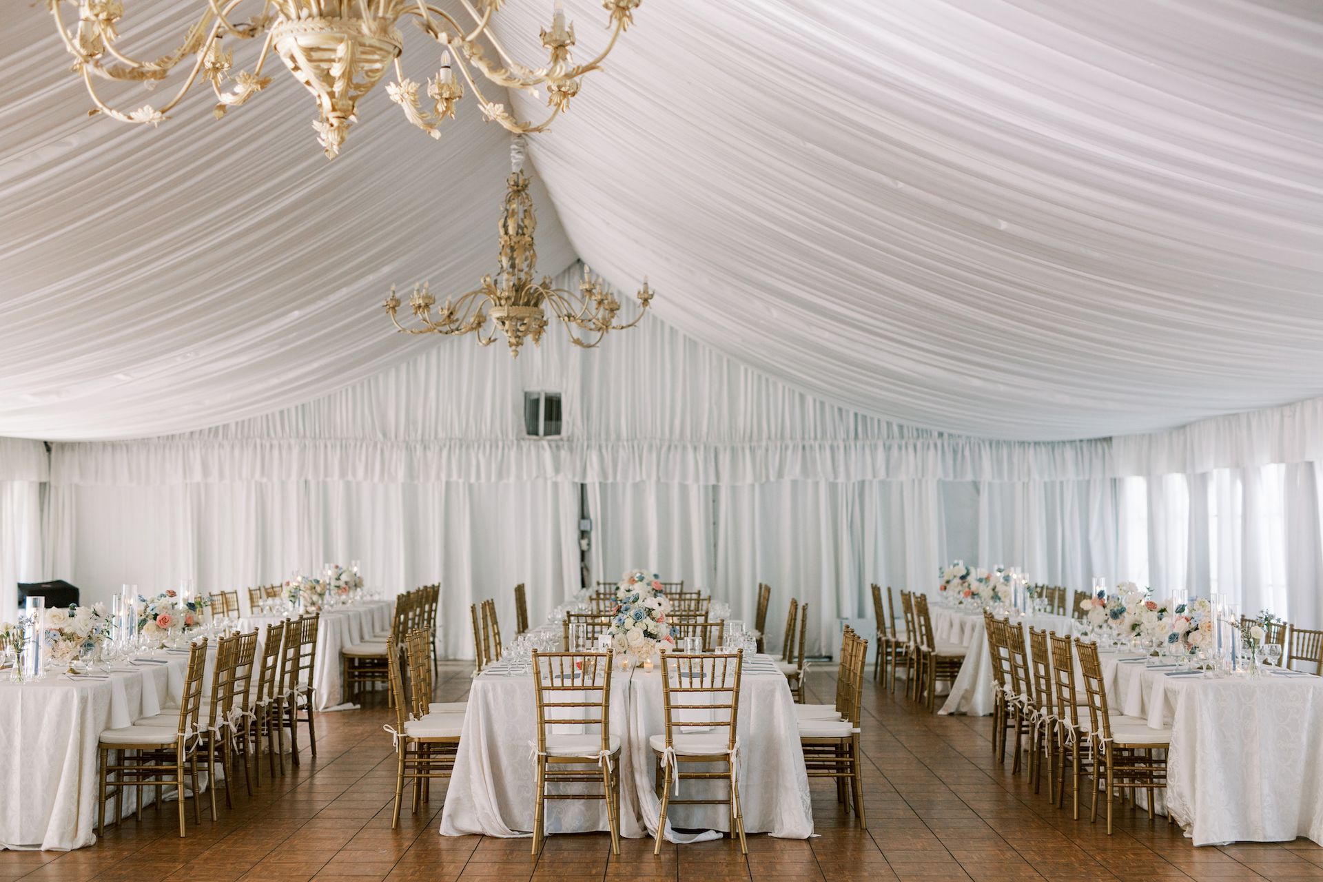 A large room with tables and chairs set up for a wedding reception under a tent.