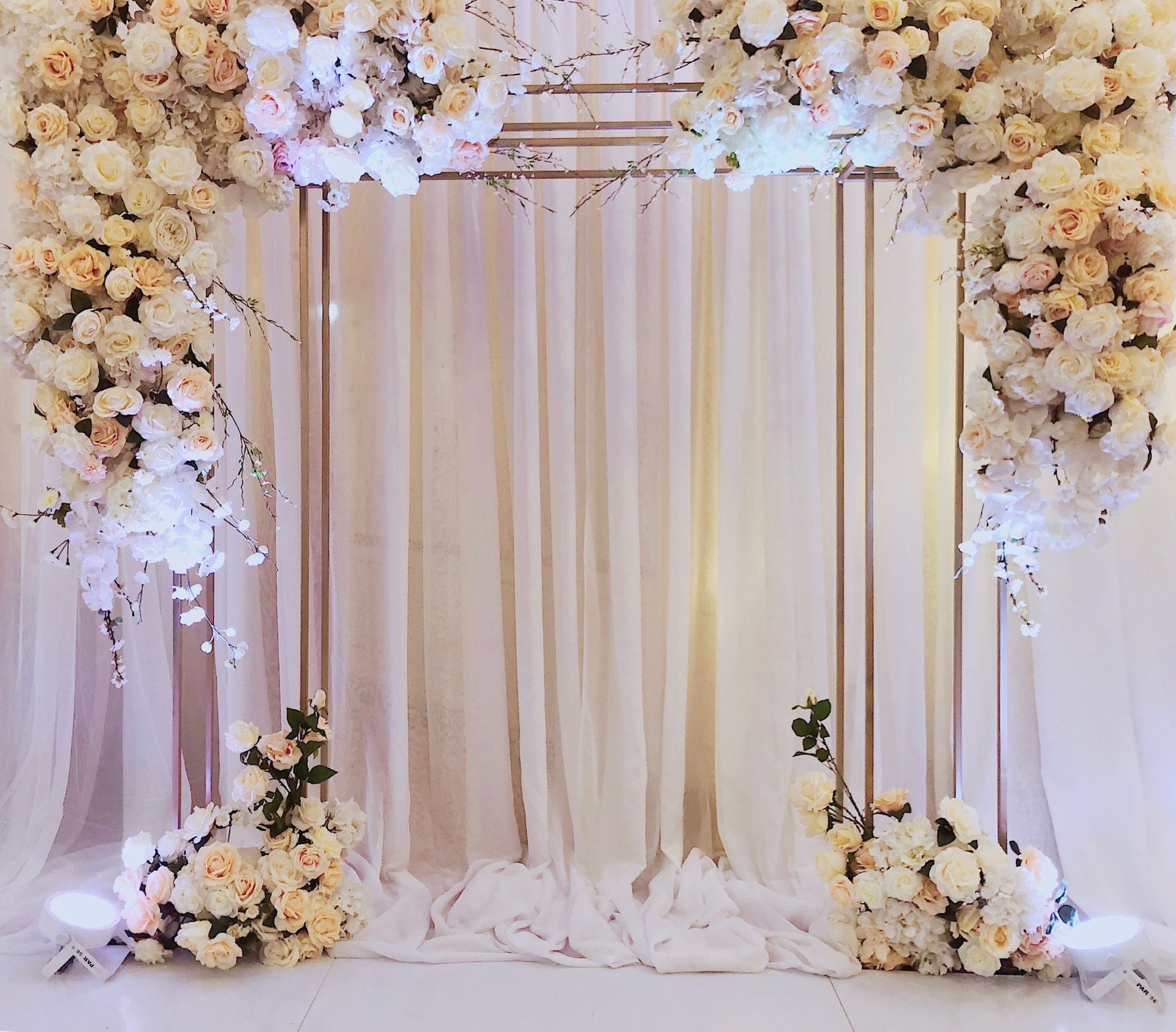 A wedding arch decorated with white flowers and a gold frame.