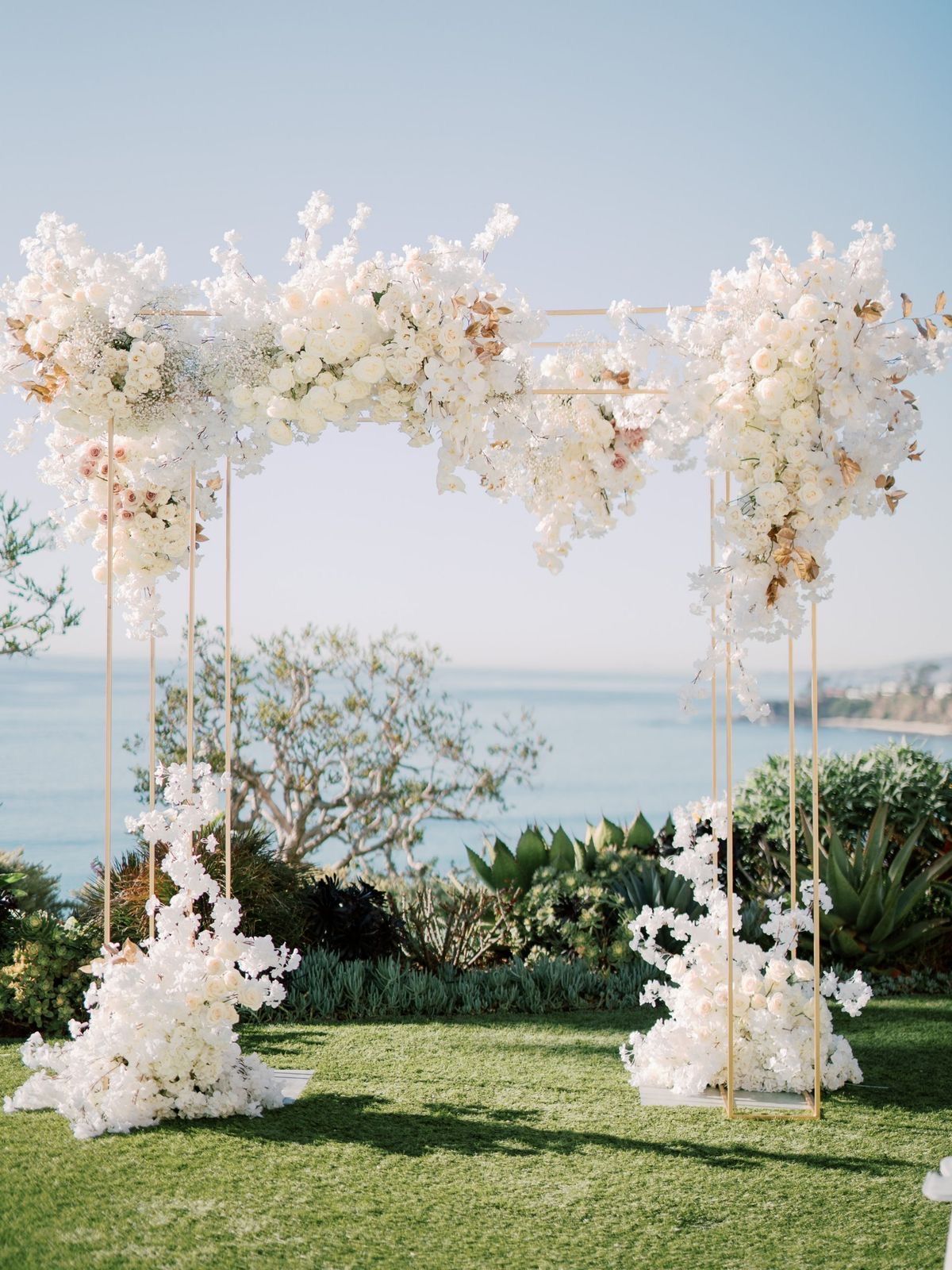 A wedding arch decorated with white flowers and a view of the ocean.