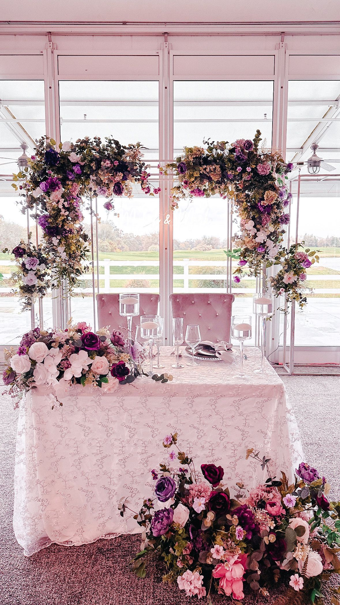 There is a table with flowers on it in front of a window.